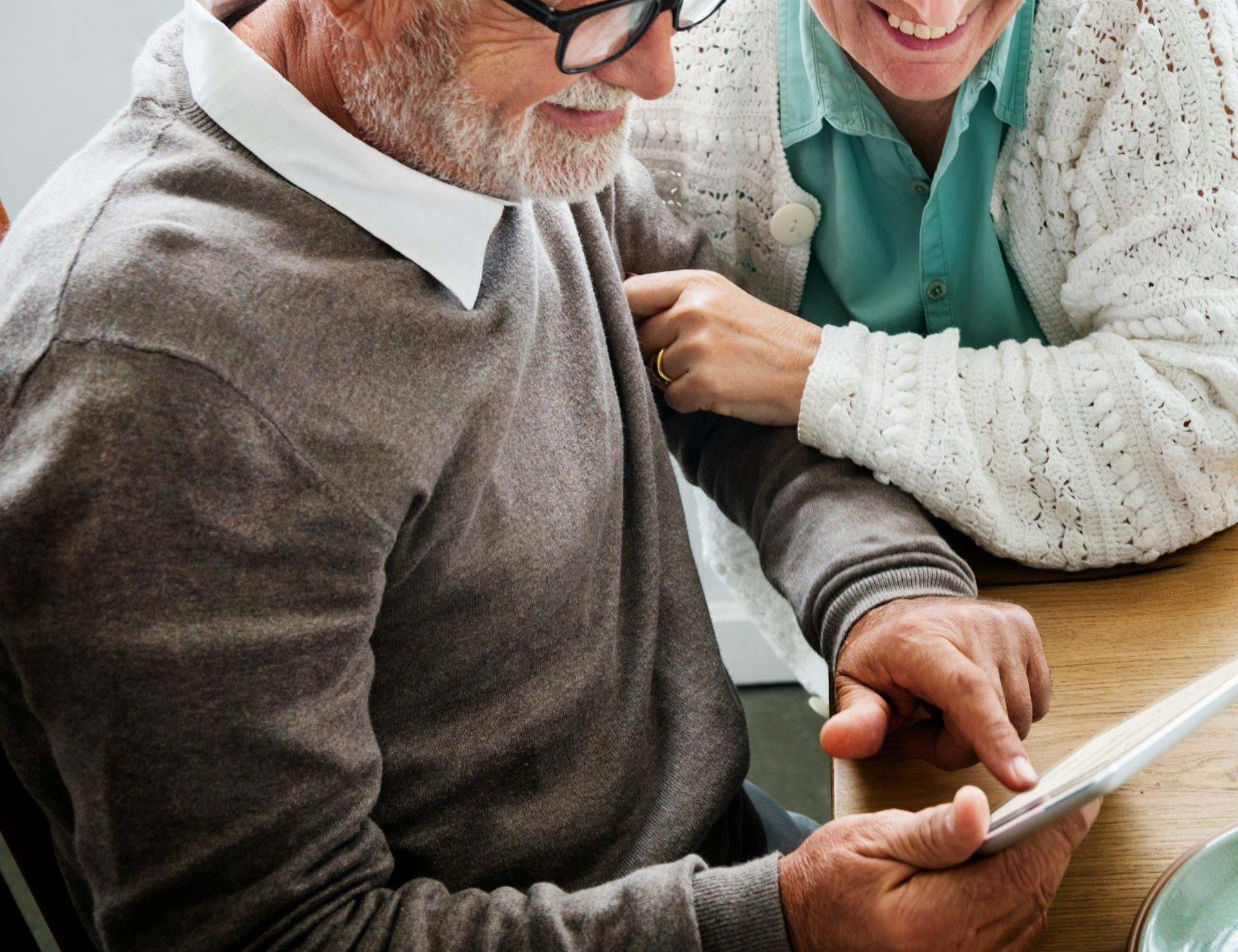 Two people smiling and looking at a tablet at a wooden table