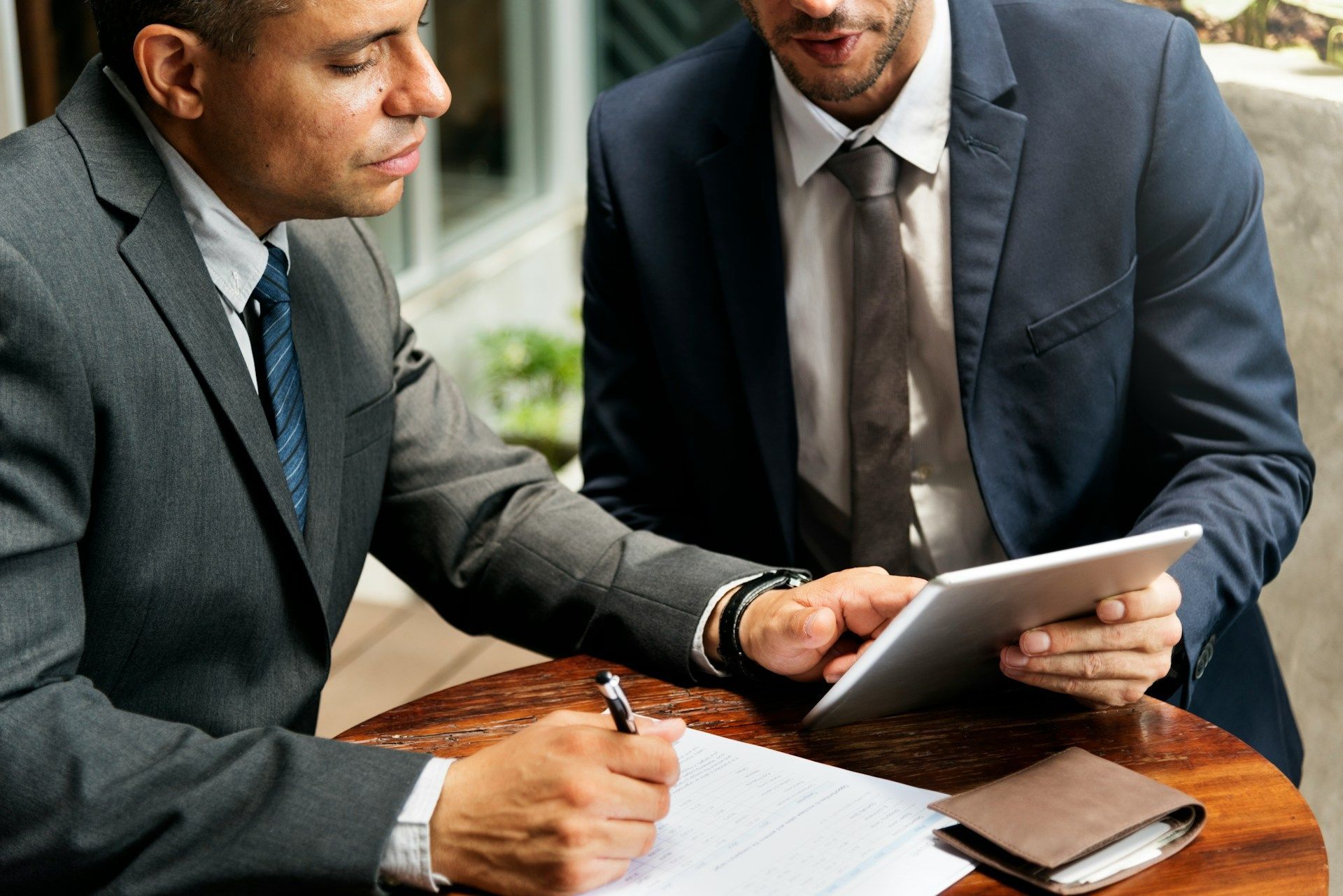 Two businesspeople reviewing a tablet and documents at a wooden table in a meeting room