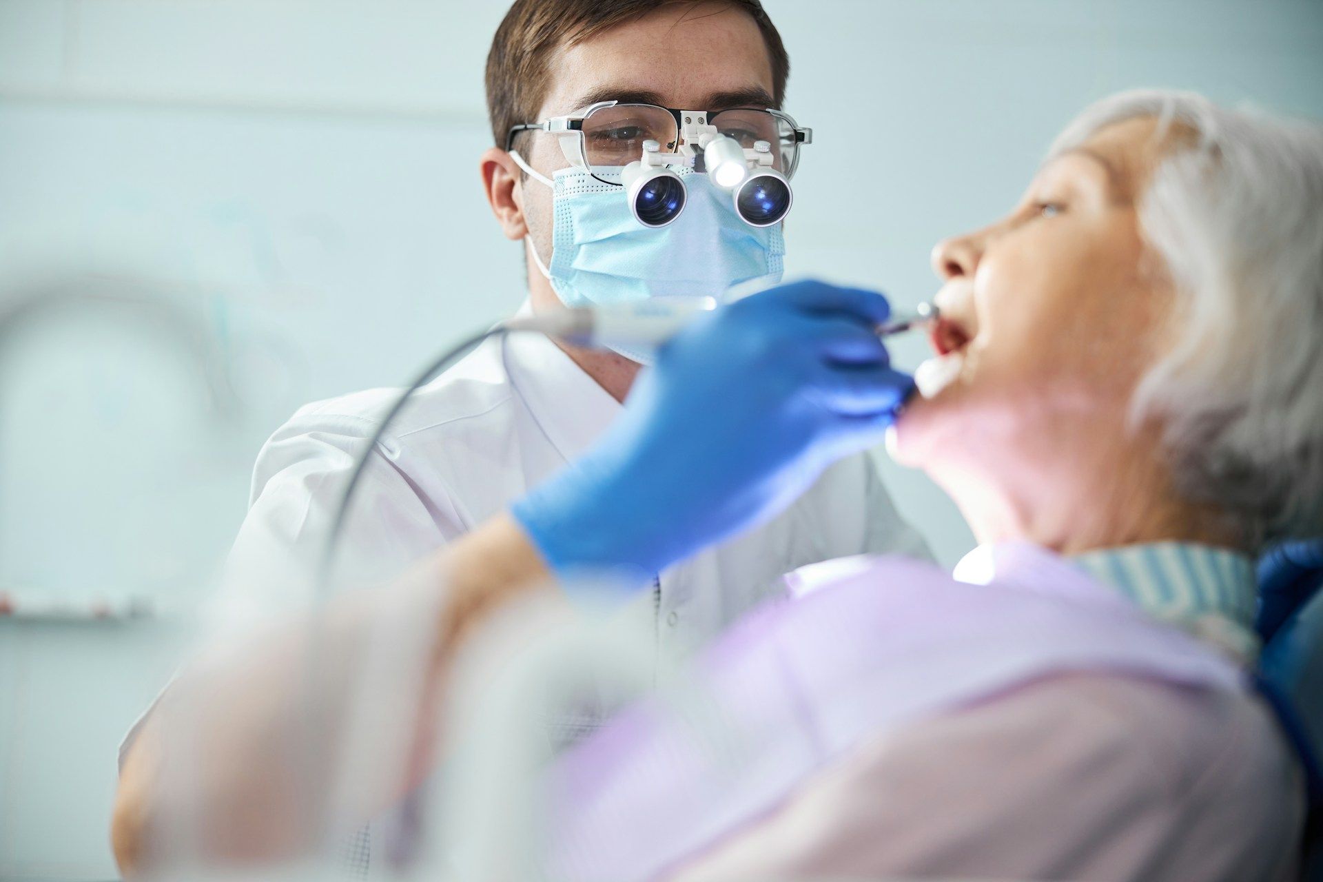 Dentist wearing mask and gloves examining a reclining patient in a dental office