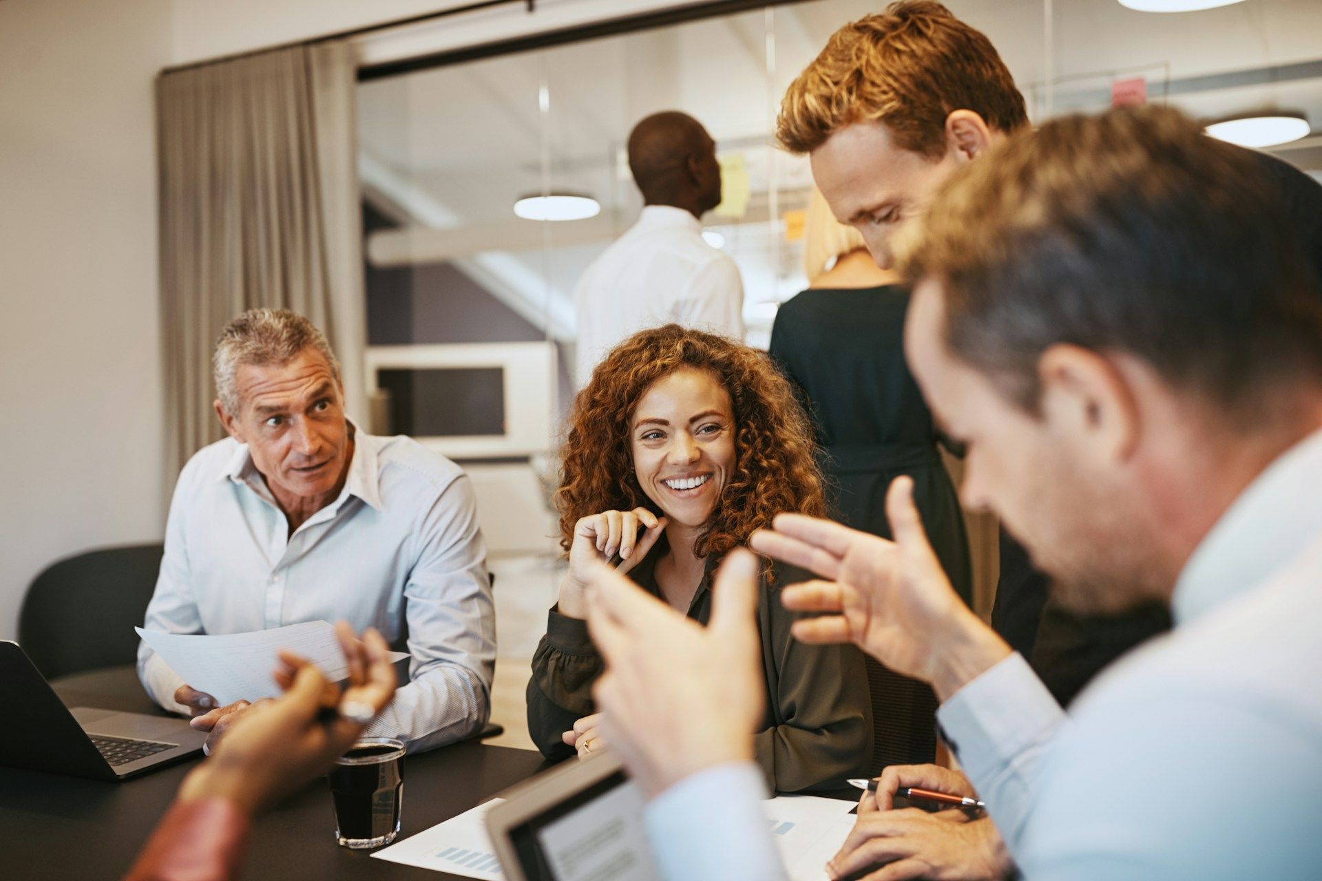 Group of coworkers in a meeting, discussing around a table with laptops in a bright office