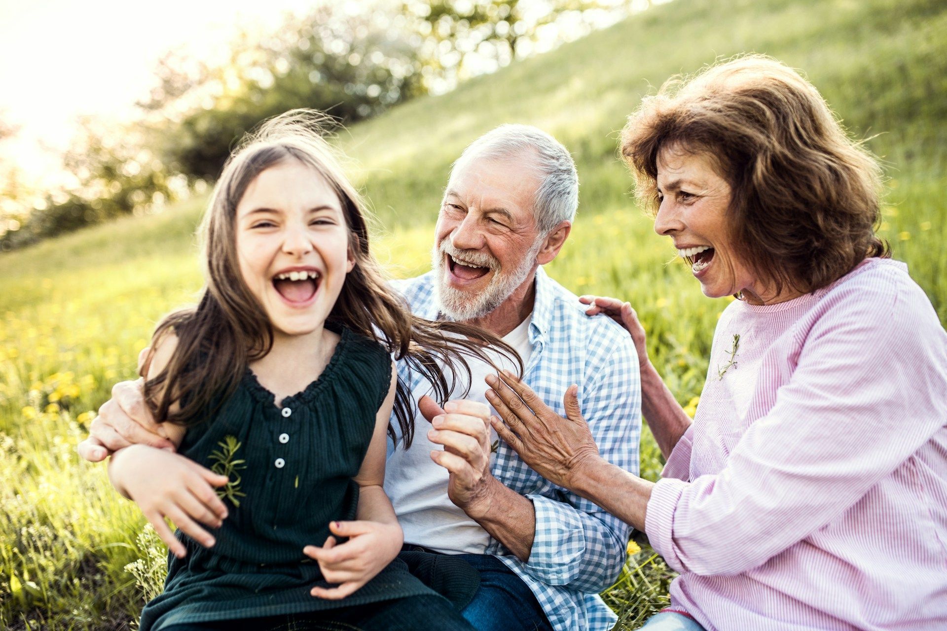 Three people laughing together outdoors in a sunny green field