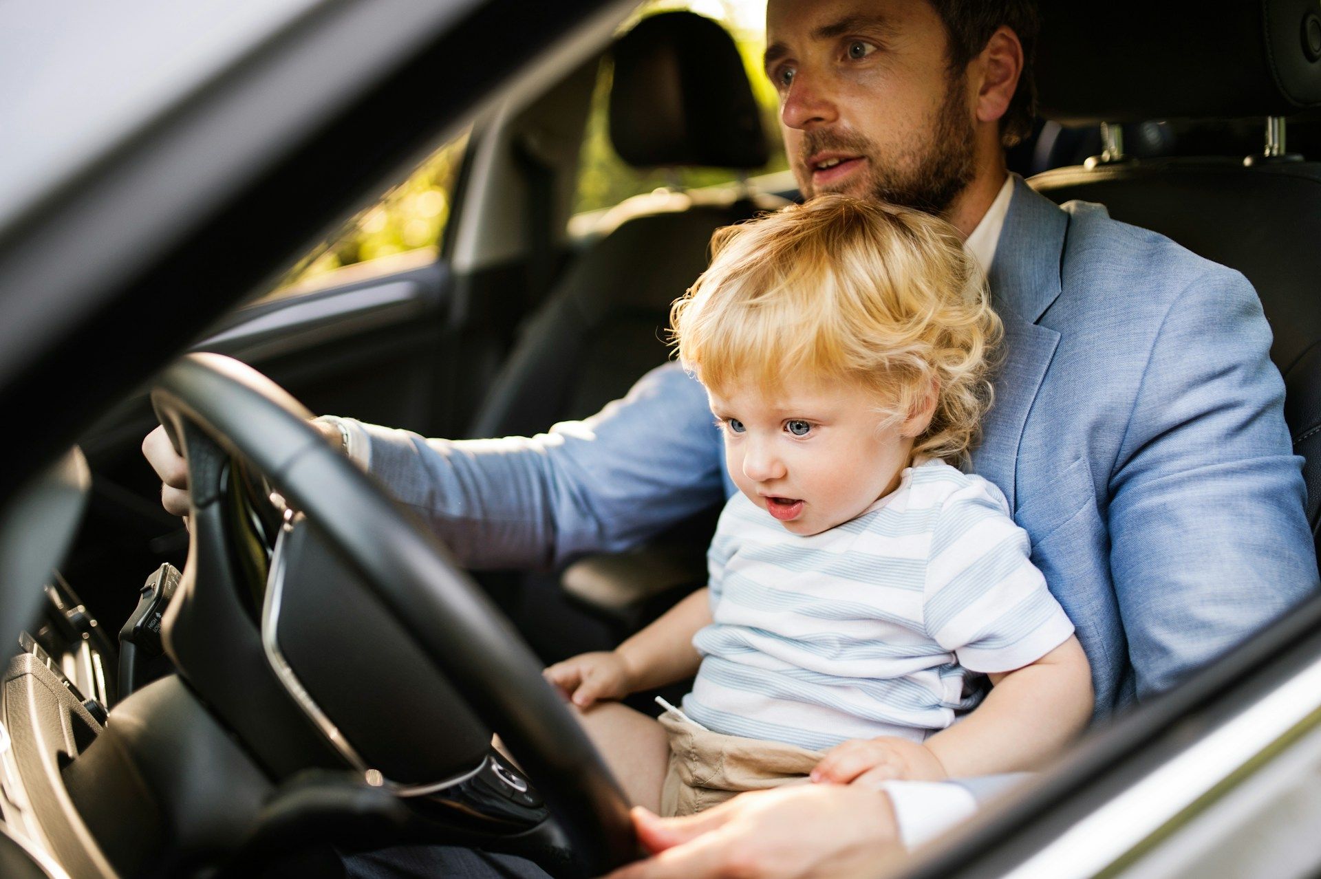 Adult and toddler sitting in a car, the adult behind the wheel watching the child in the front seat