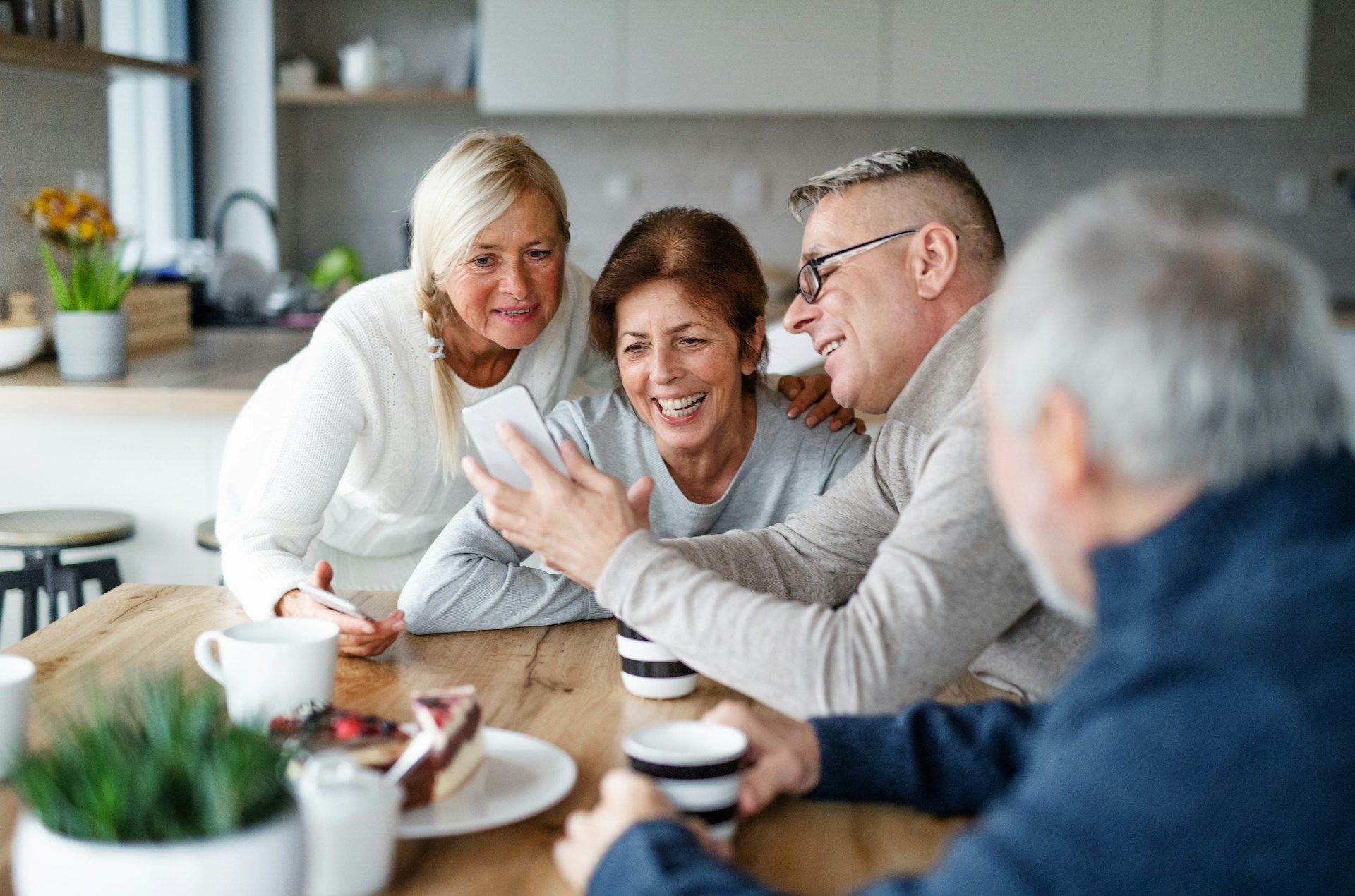 Friends chatting over coffee at a kitchen table, smiling and gesturing in a bright home setting