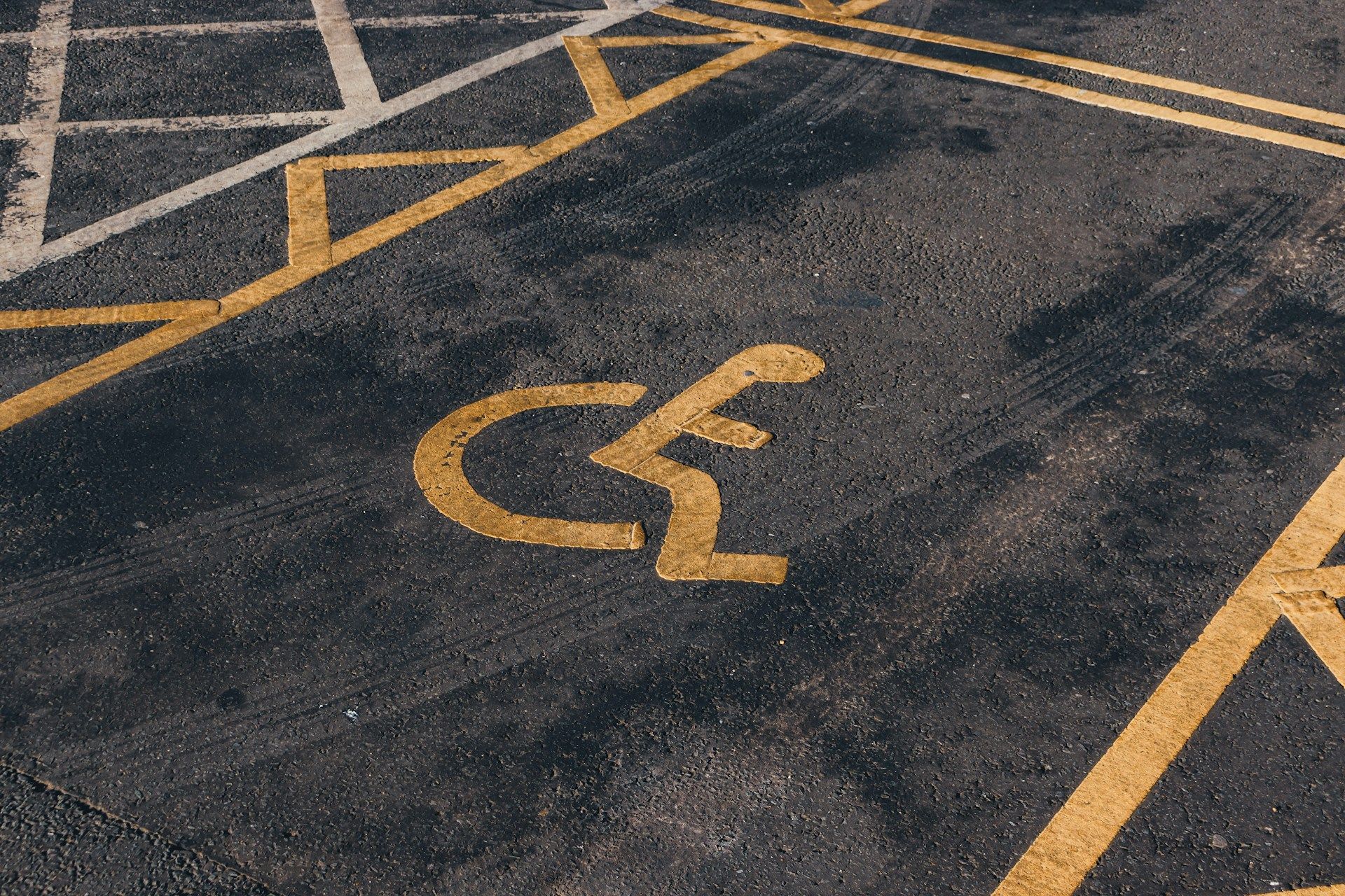 Handicap parking space symbol painted in yellow on dark asphalt with diagonal parking lines