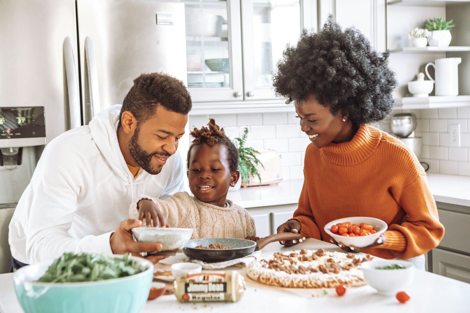Family baking together in a bright kitchen, smiling and decorating a cake with bowls of ingredients nearby.