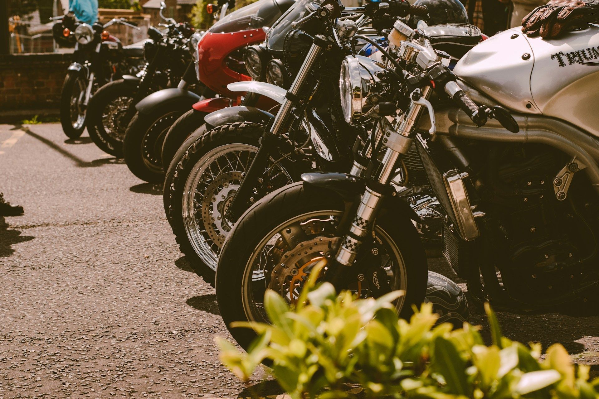 Parked motorcycles lined up on a sunlit street, with a white bike in the foreground.
