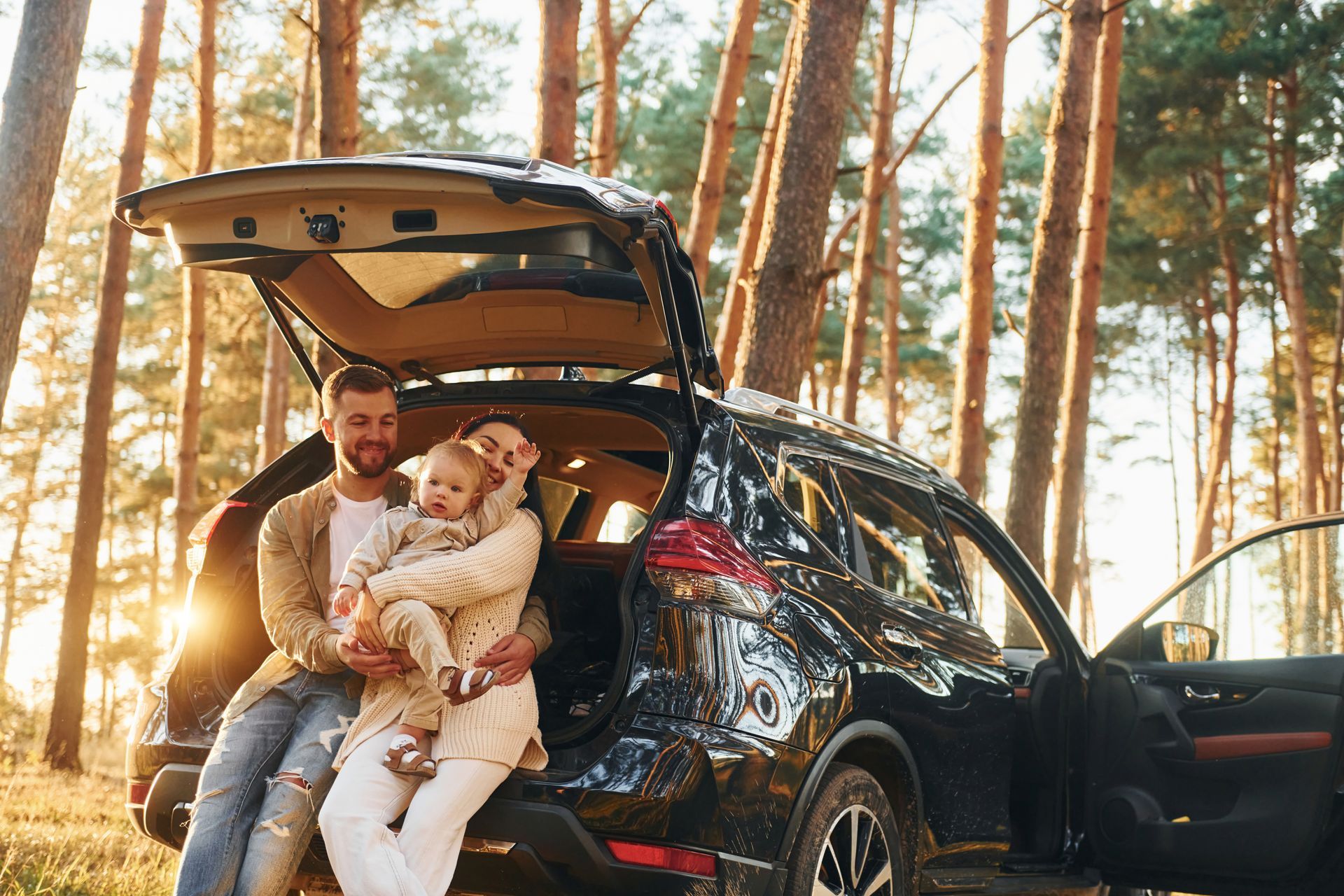 Family sitting by open SUV hatch in a pine forest at sunset