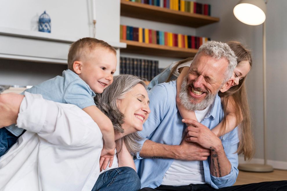 Smiling family relaxing on a couch in a bright living room, with a child hugging an adult from behind