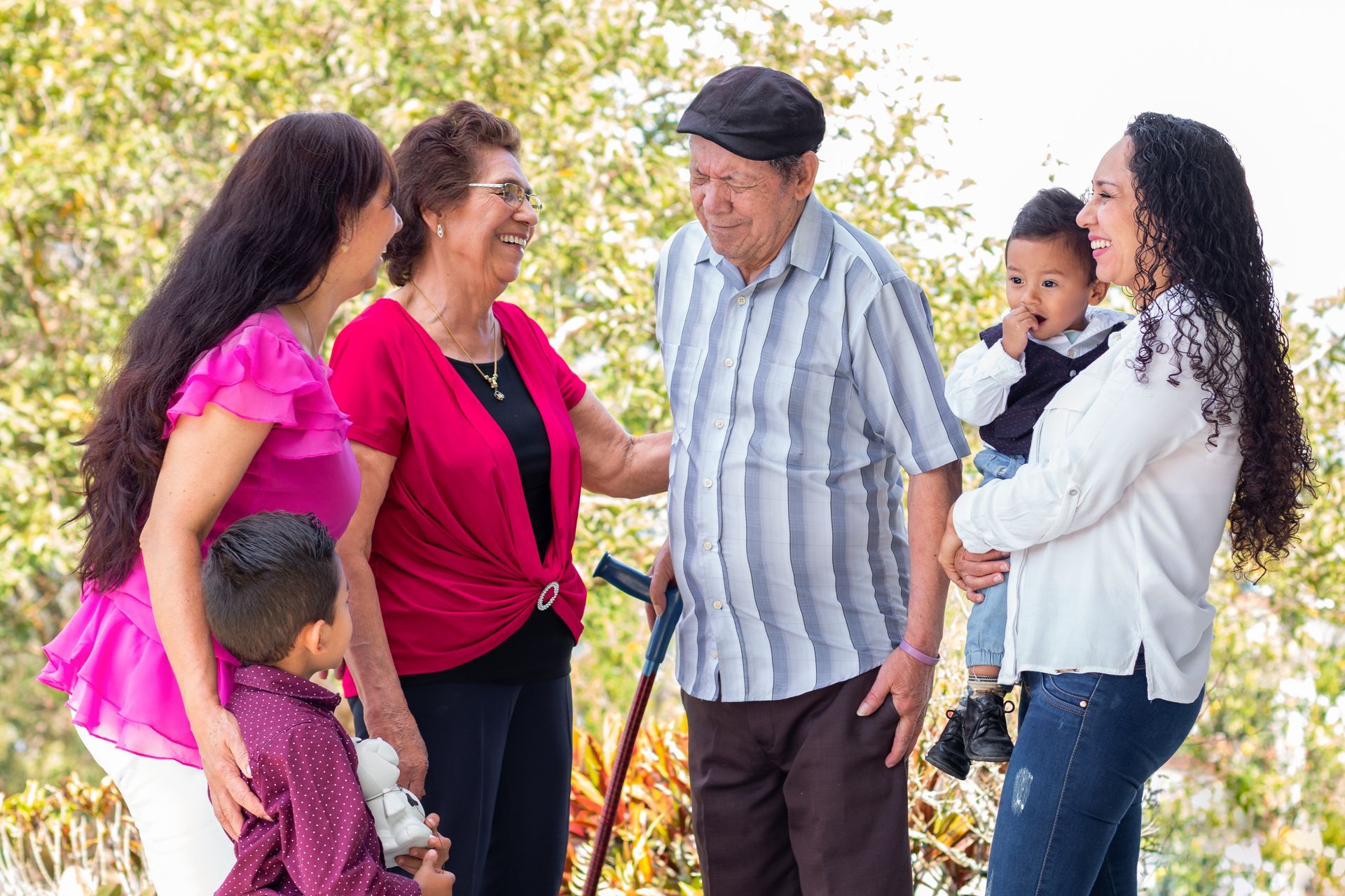 Five people chatting outdoors, with two adults holding small children in a bright, sunny setting