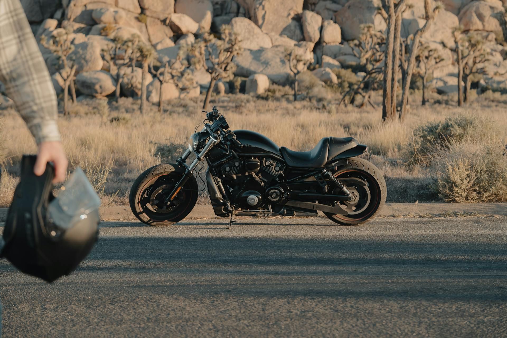Black motorcycle parked on a road beside a rocky desert with sparse trees