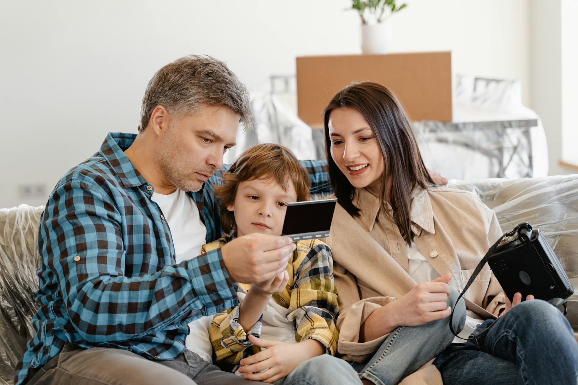 Family sitting on a couch, looking at a tablet together in a bright living room.