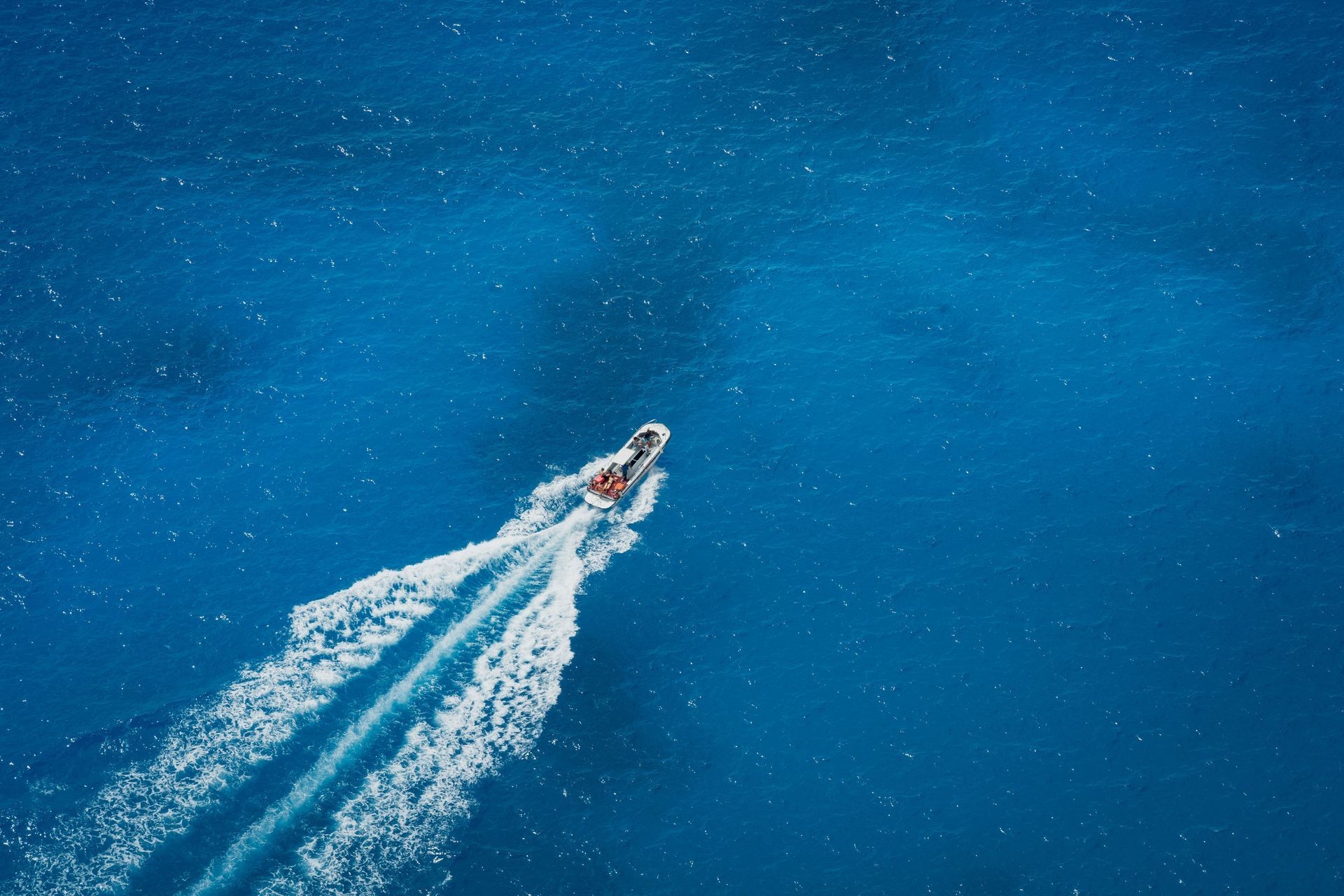Small motorboat speeding across bright blue water, leaving a white wake behind