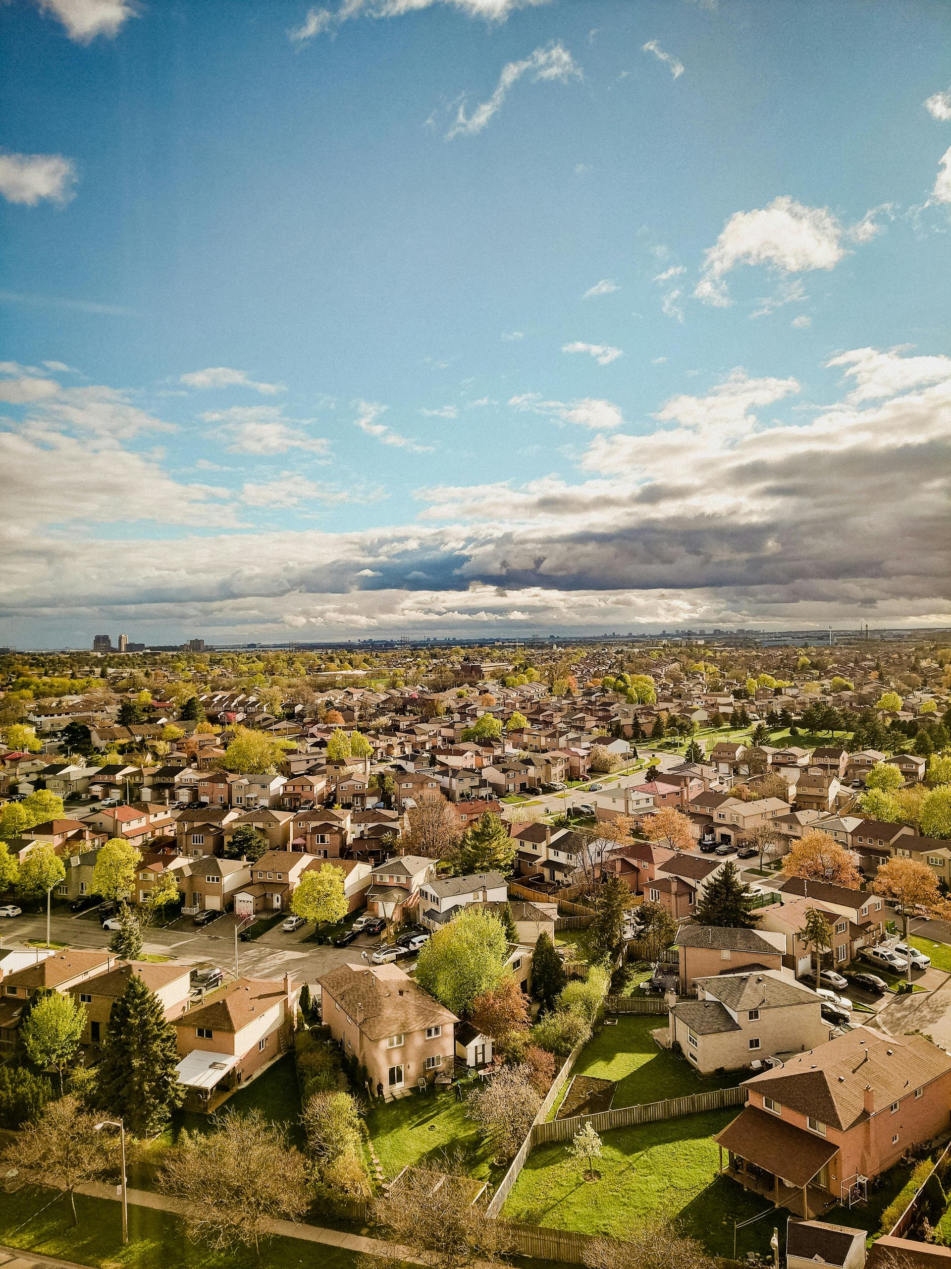 Aerial view of a suburban neighborhood with rows of houses, green trees, and a partly cloudy sky