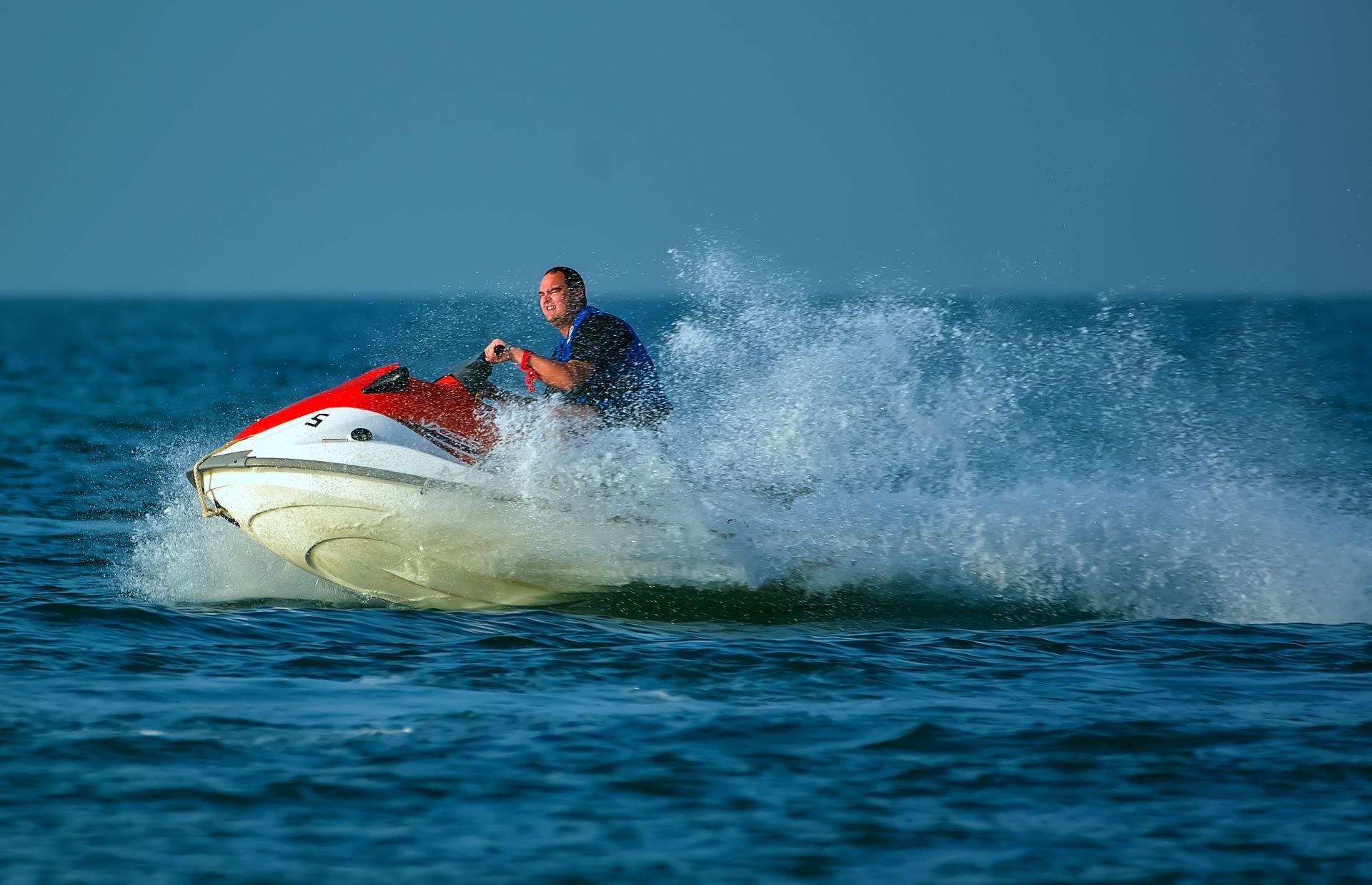 Person riding a red-and-white jet ski, splashing across the blue ocean.