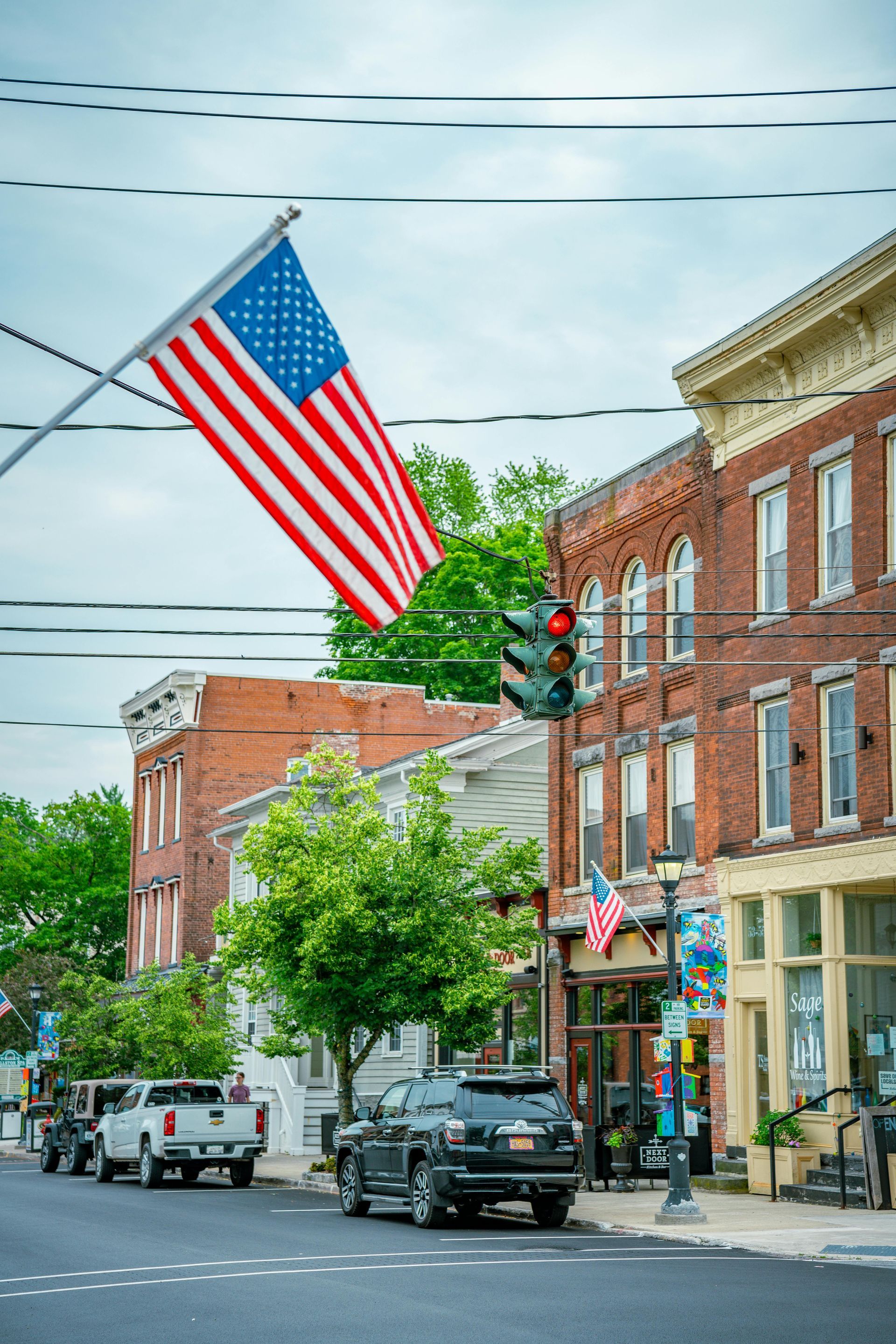 Downtown street with a large American flag hanging overhead and brick storefronts along the sidewalk