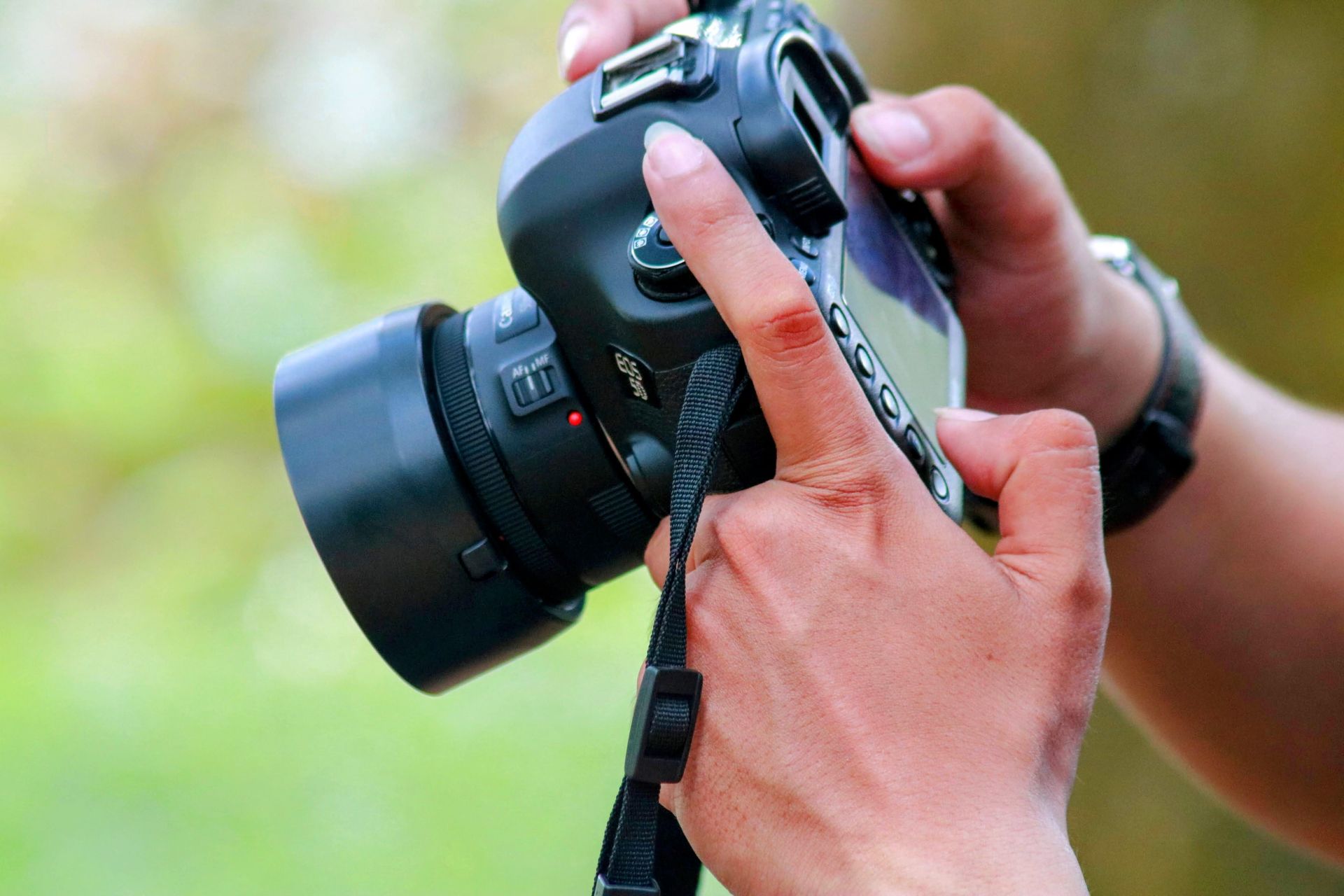 Hands adjusting settings on a black DSLR camera with lens outdoors.