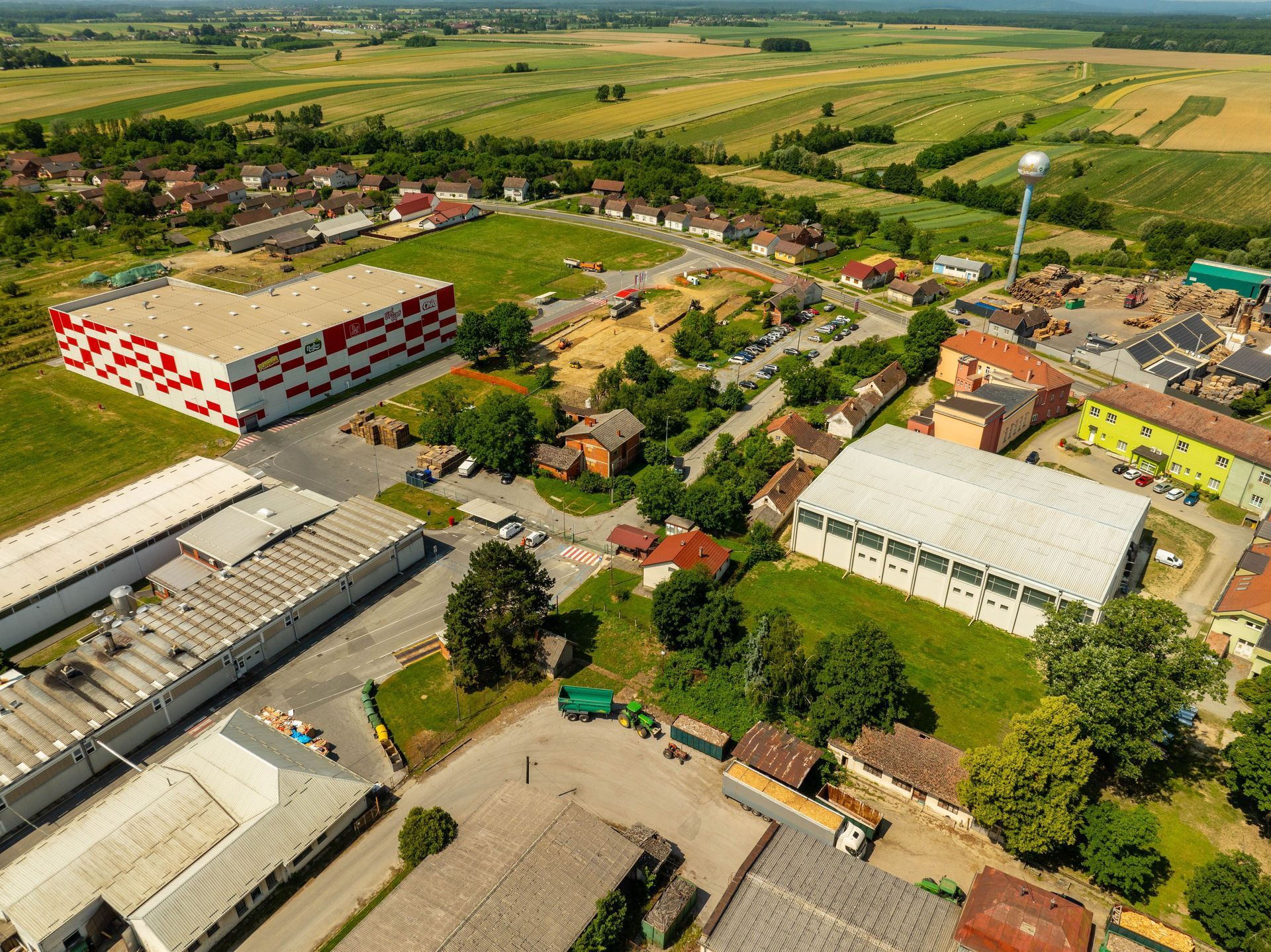Aerial view of a rural village with homes, trees, fields, and industrial buildings under a clear sky