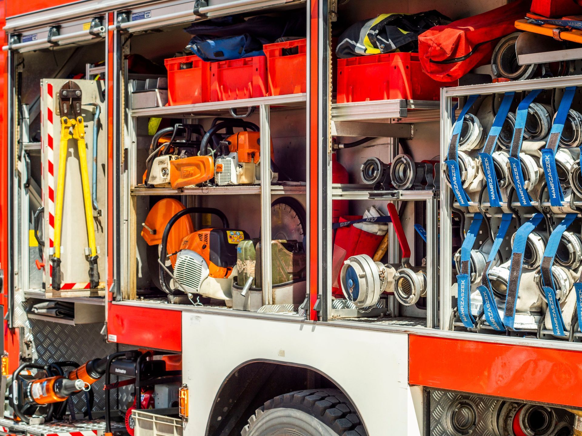 Open fire truck compartments packed with hoses, tools, and equipment in bright red and silver.