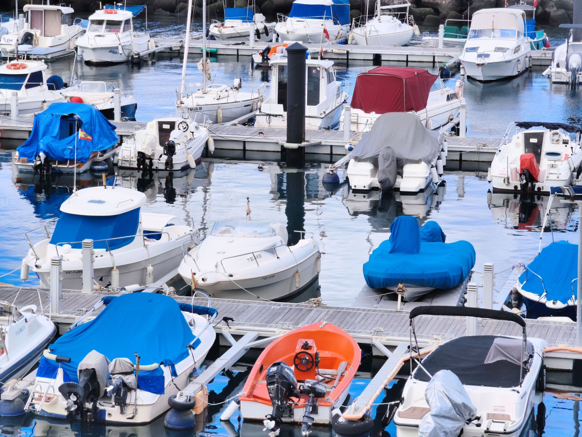Snow-covered boats moored in a marina, many covered with blue tarps and reflecting on wet water.