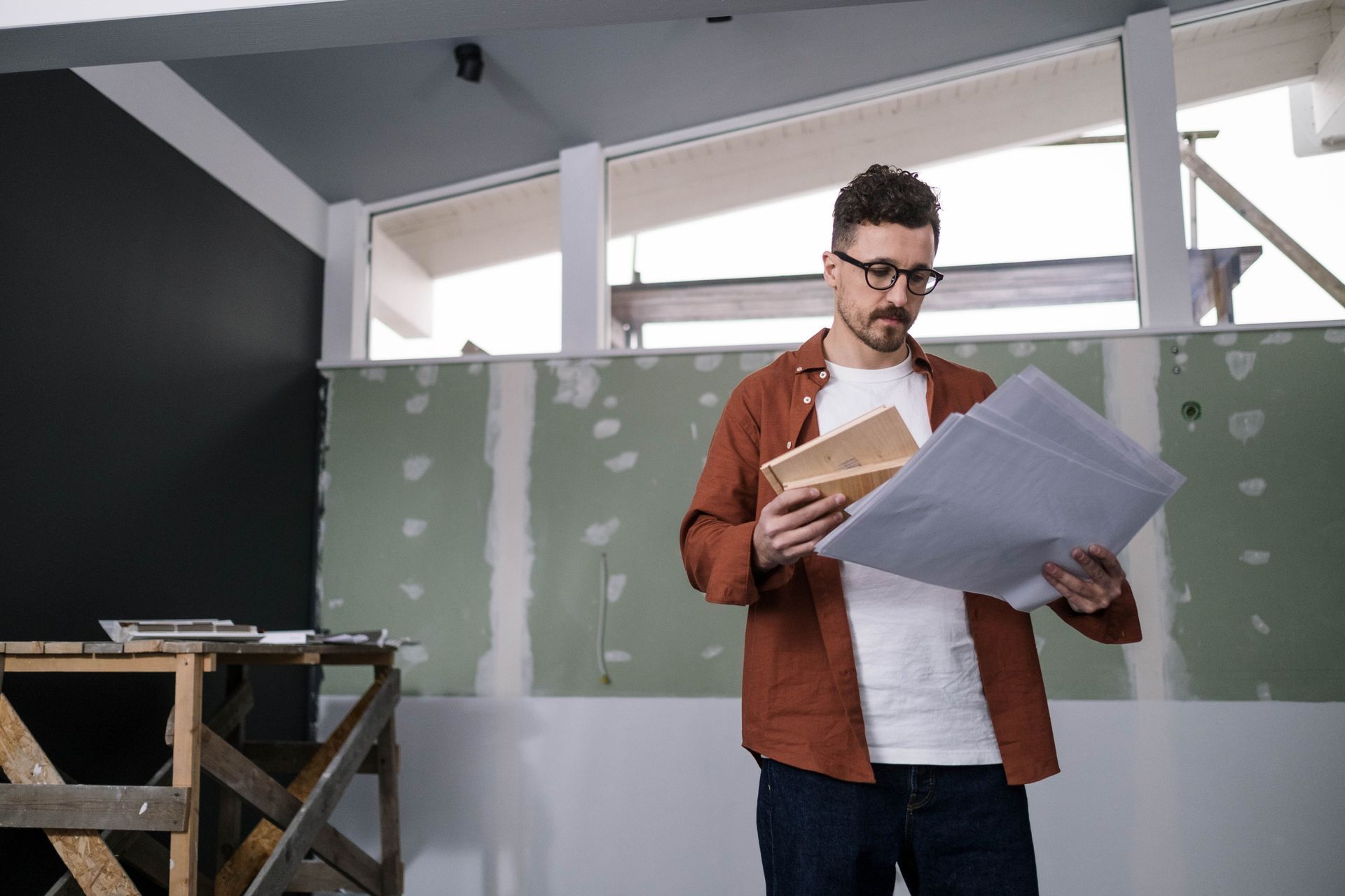 Man examining blueprints in a partially renovated room with green walls and a workbench