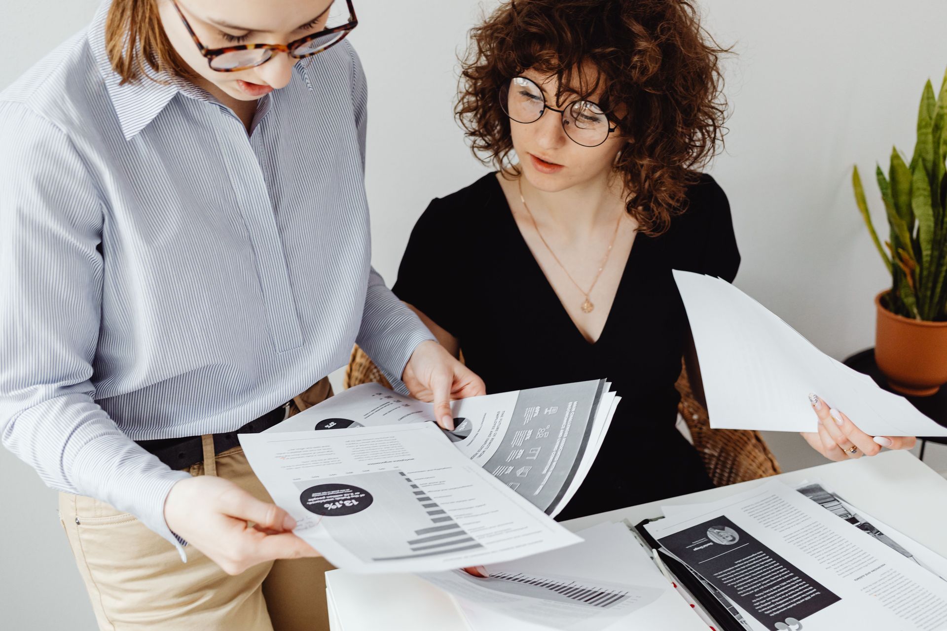 Two coworkers reviewing printed documents at a desk in a bright office