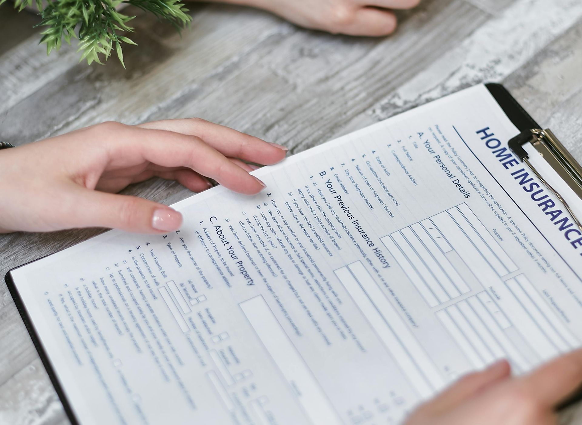 Hands reviewing a home insurance form on a wooden table, with a pen and coffee nearby.