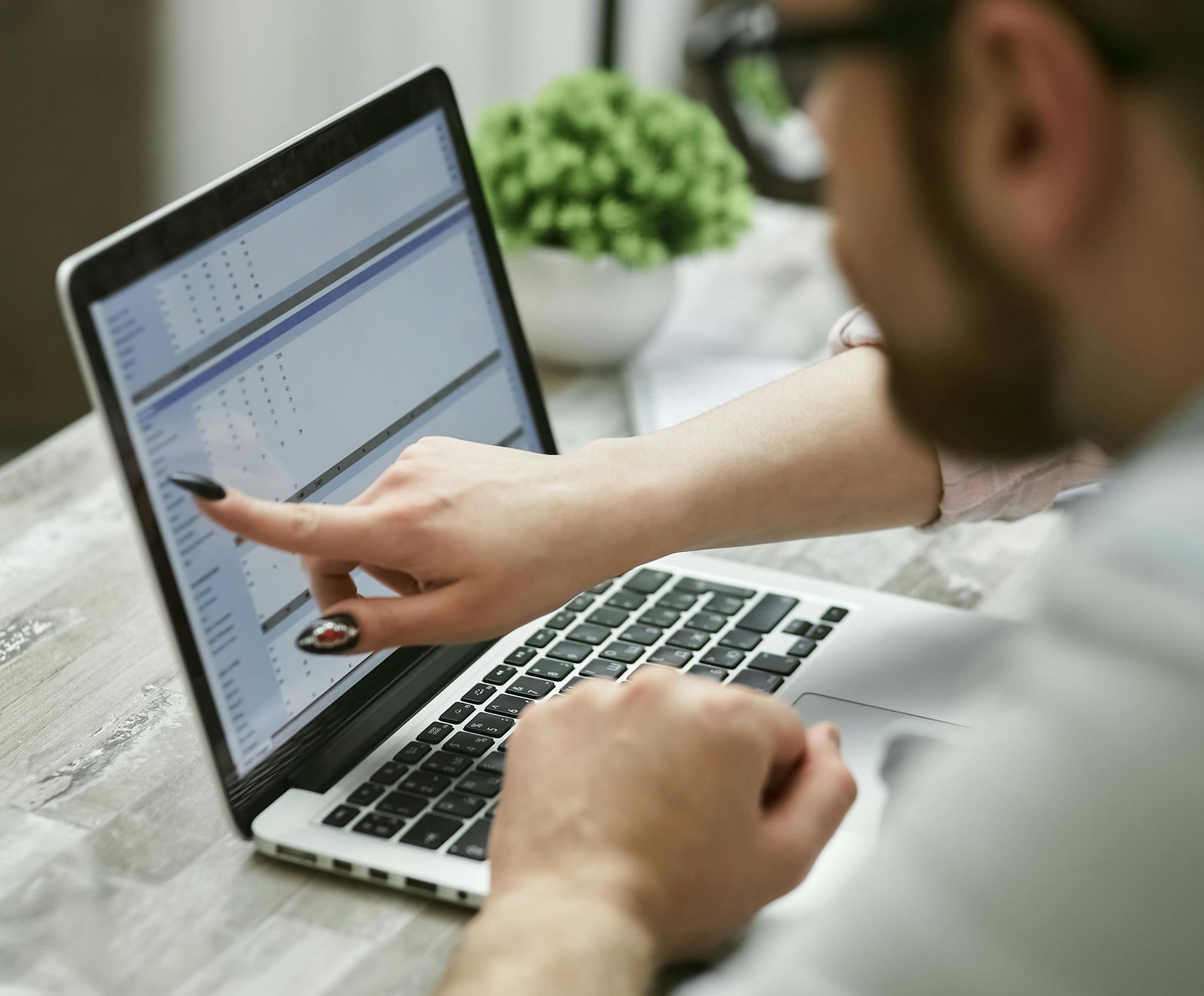 Person pointing at a laptop screen with charts and text on a desk