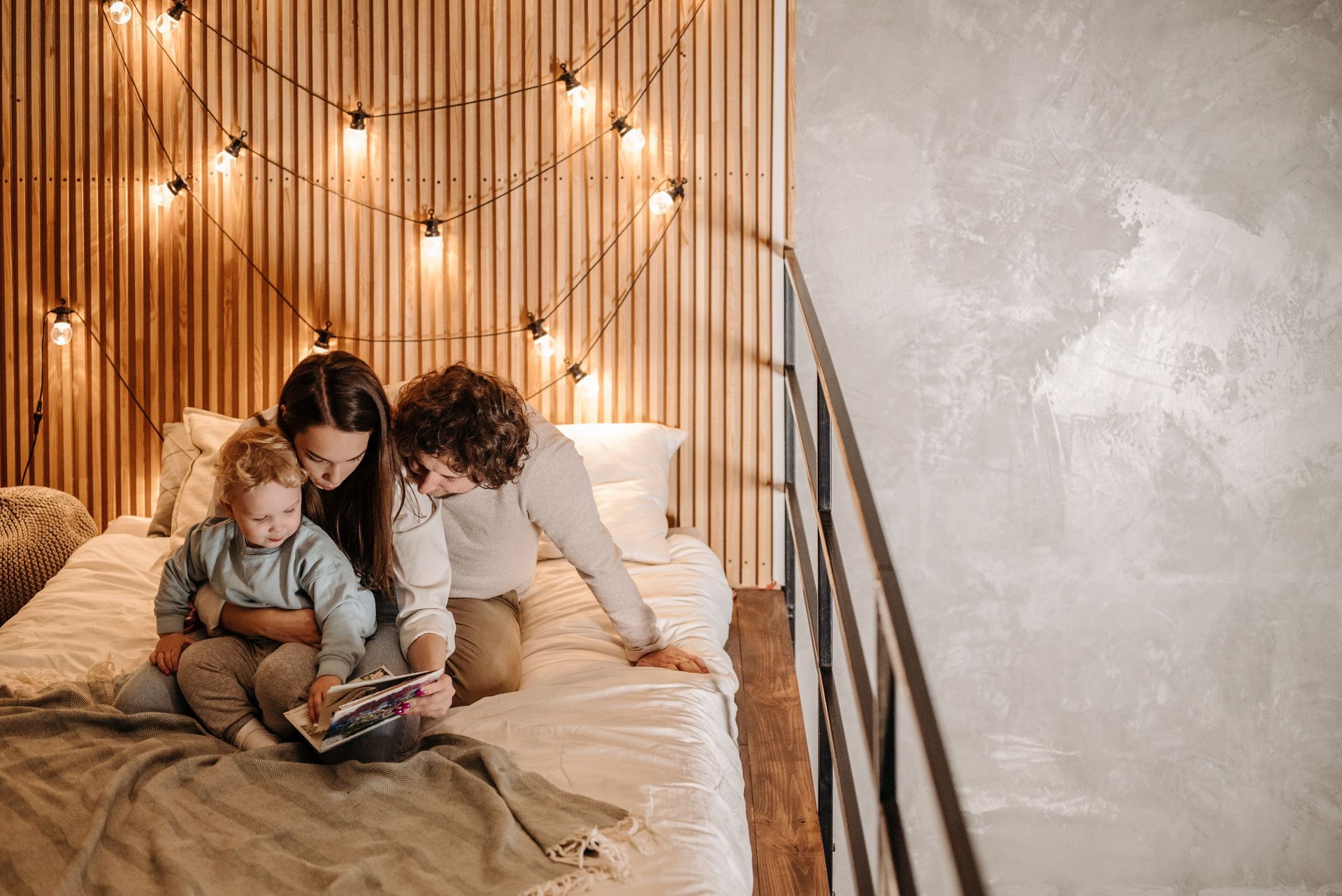 Adult and child sitting on a bed, reading together under warm string lights in a cozy bedroom.