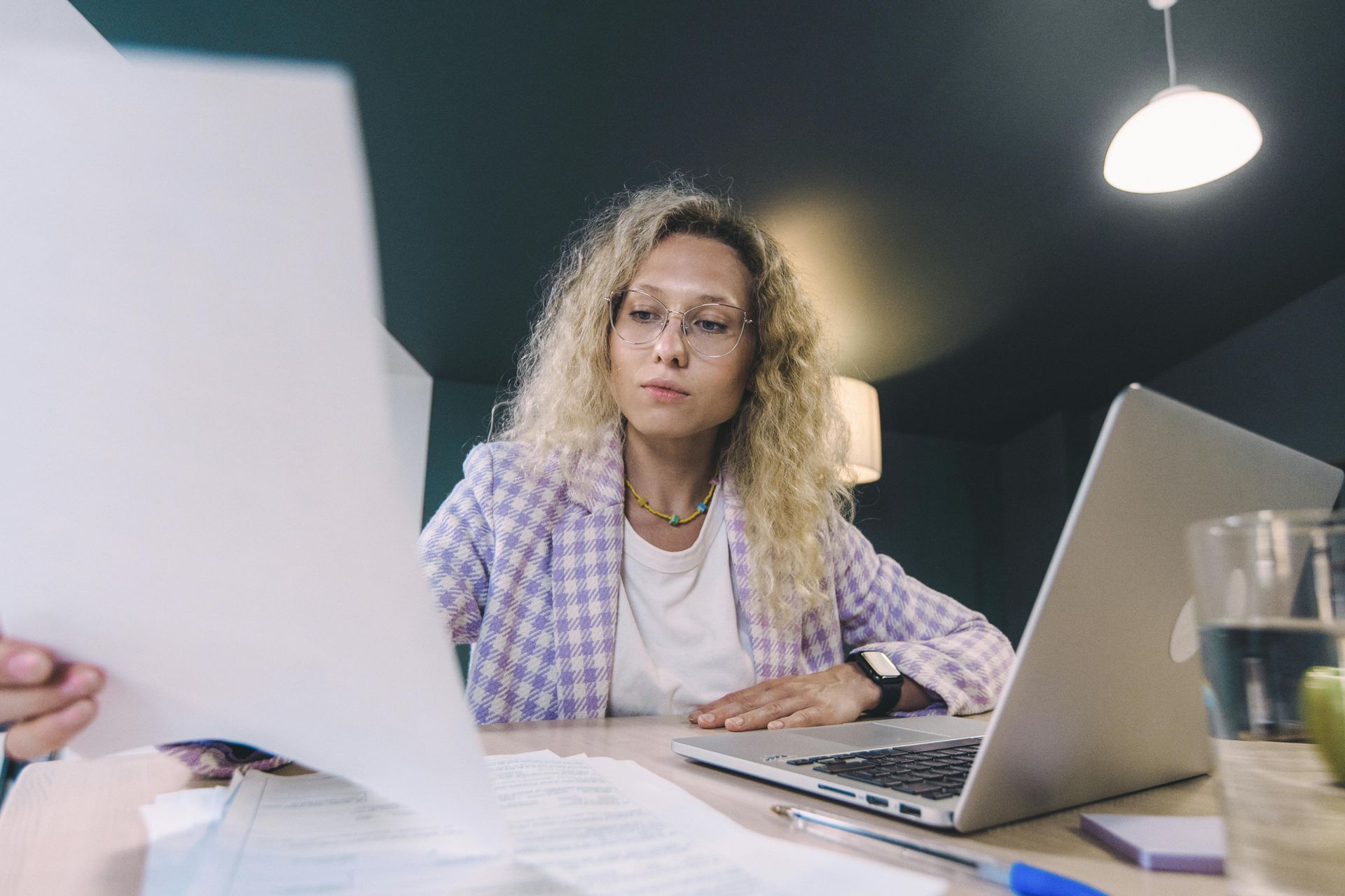Person working at a laptop and reviewing papers in an office setting