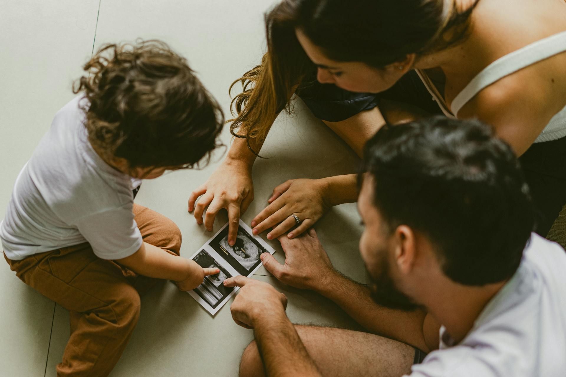 Four people gathered on a floor, reviewing printed photos together in a warm indoor setting.