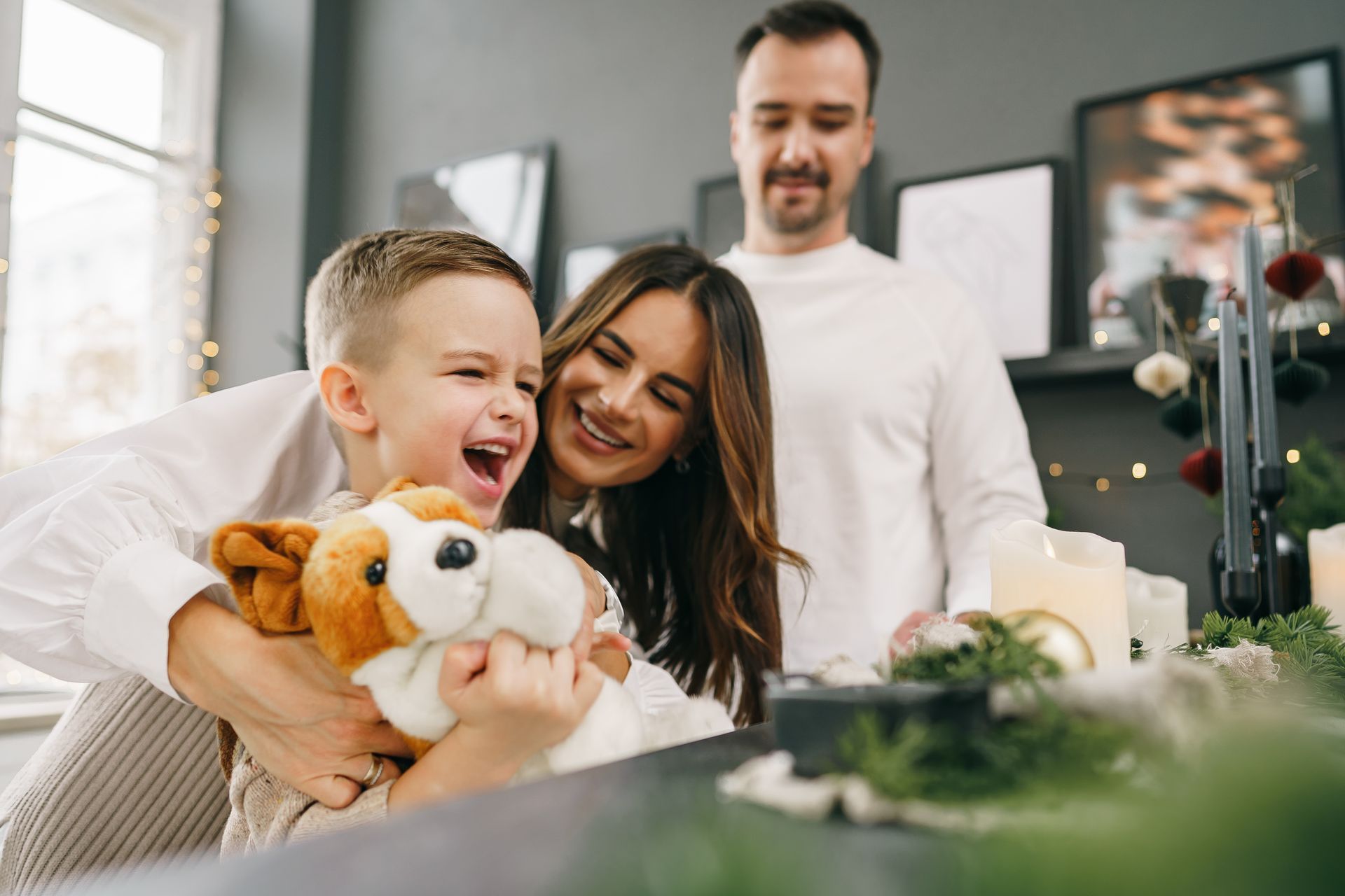 Smiling family with plush toys in a bright living room, child hugging a stuffed dog.
