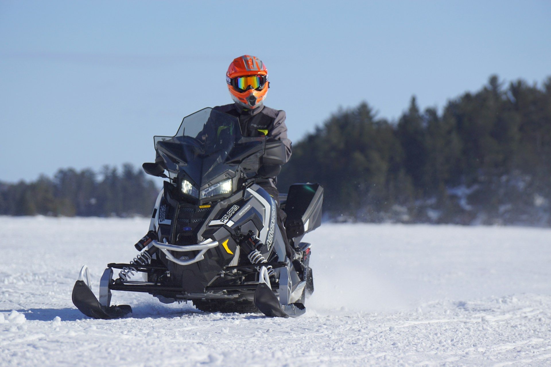 Person riding a black snowmobile across snowy terrain under a clear blue sky