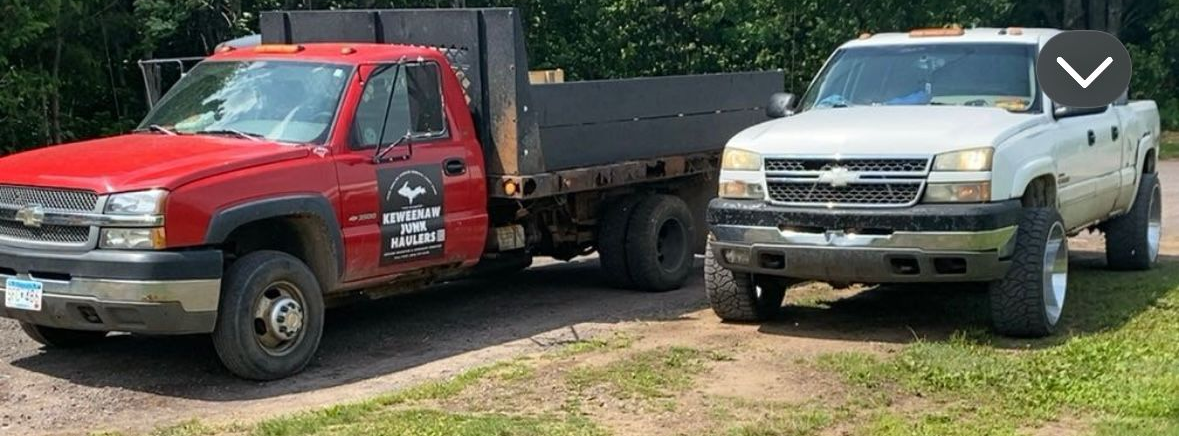 Two pickup trucks parked outside. One red dump truck, one white pickup truck.