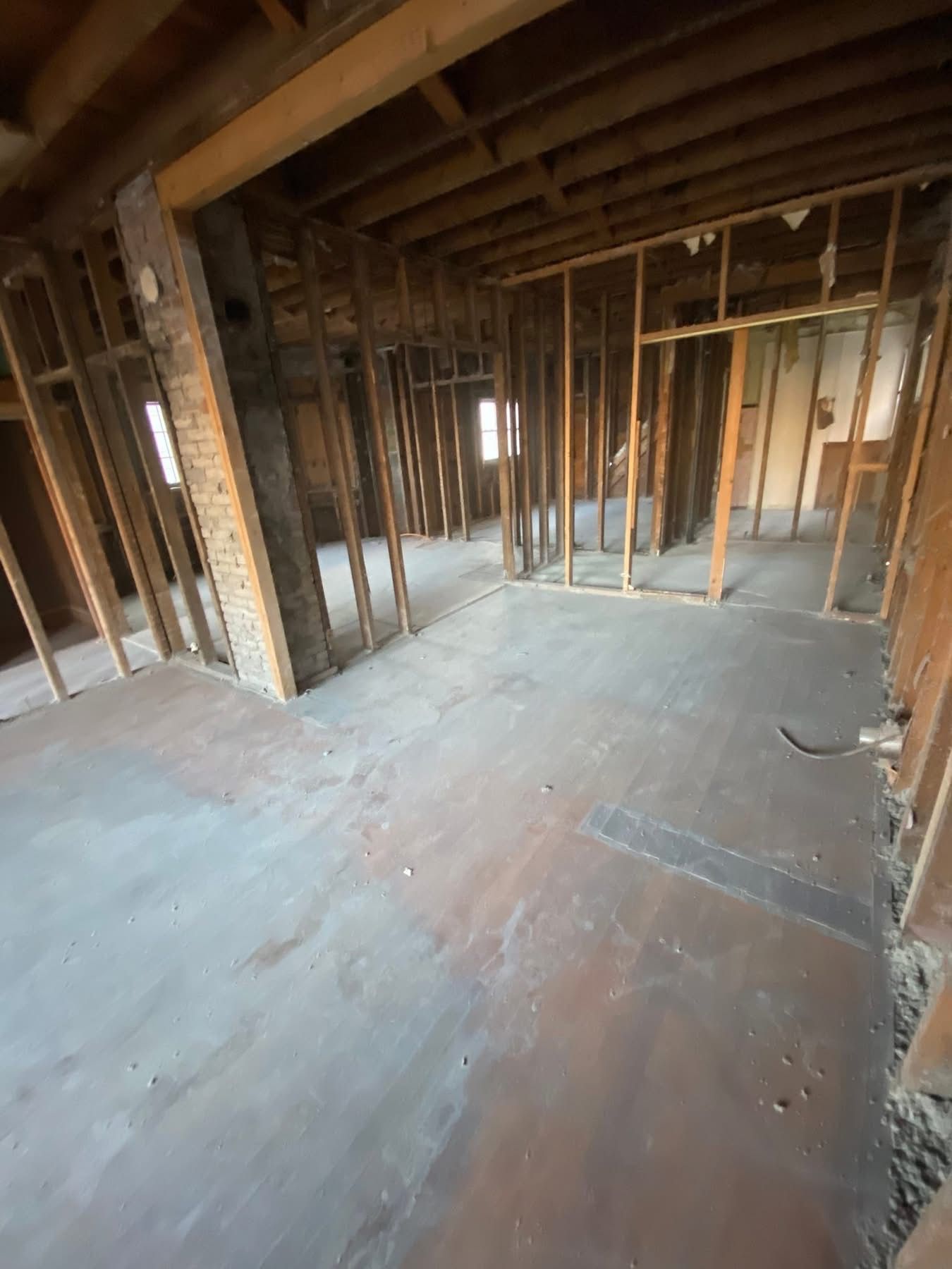 Interior of a building under renovation, showing exposed wooden framing and concrete floor.