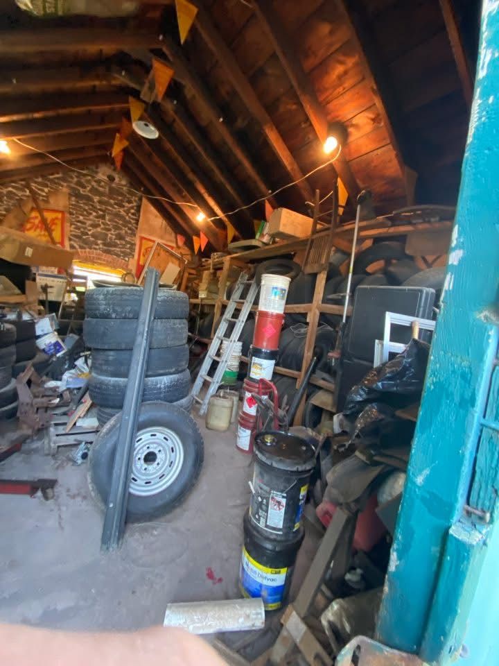 Cluttered attic with tires, paint cans, and various objects. Wooden beams and a small ladder are visible.