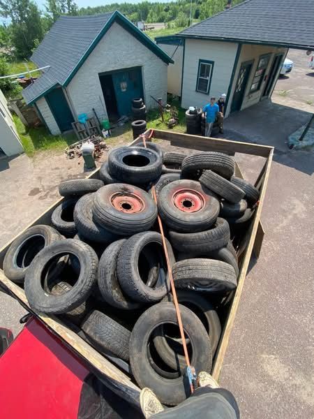 Wooden bin overflowing with tires in front of two buildings. People are visible nearby.