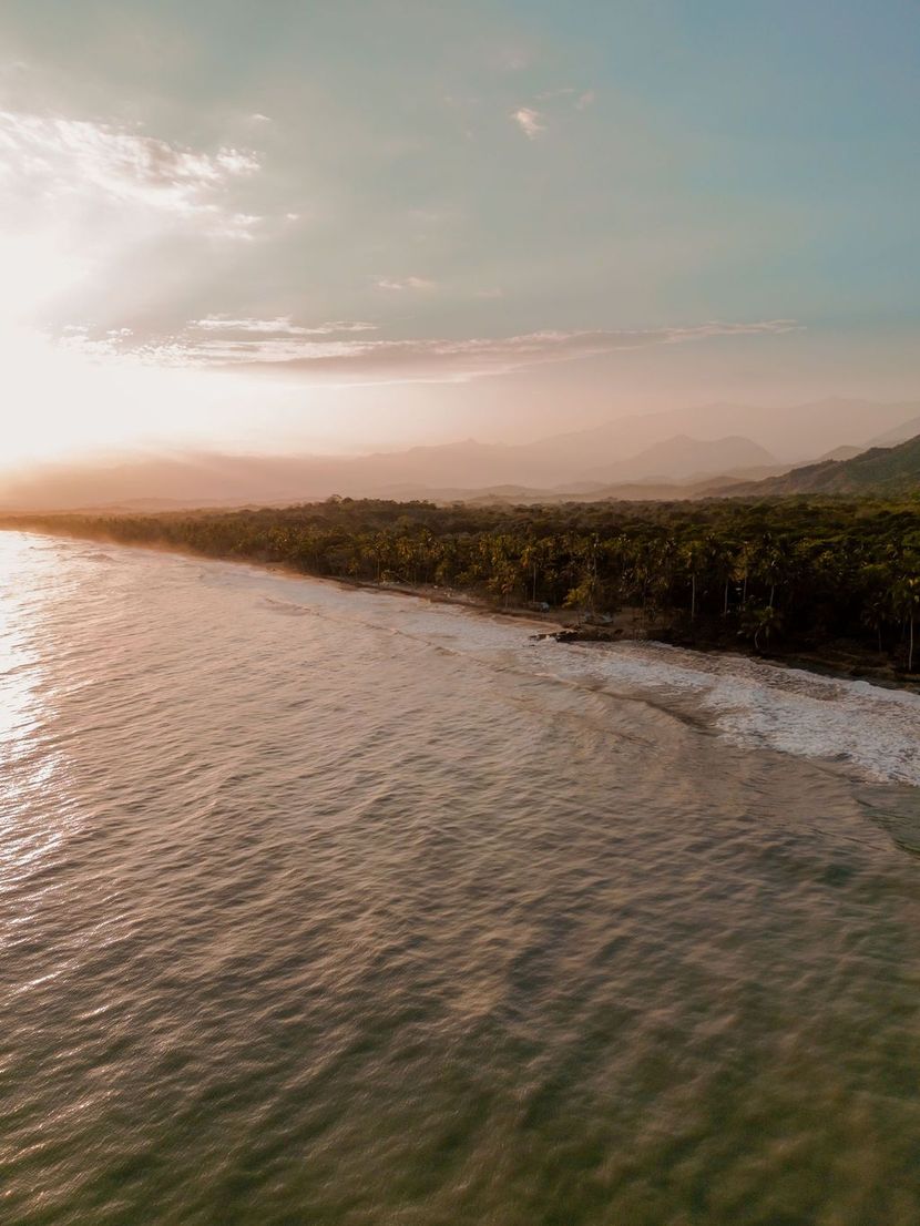 Vista aérea de una costa tranquila al atardecer, con agua ondulante y una costa verde a lo lejos.