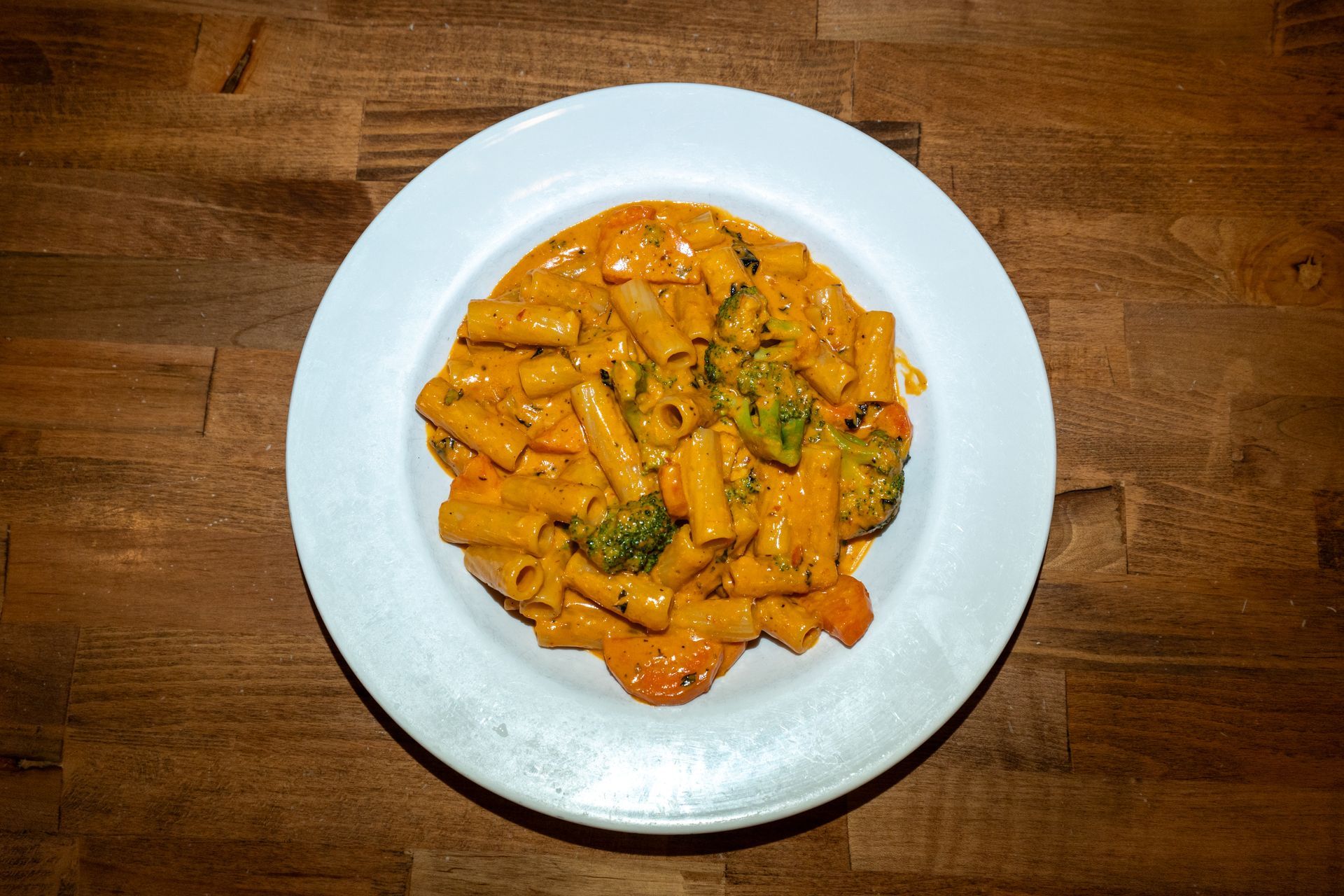 Pasta dish with rigatoni, broccoli, and a creamy orange sauce, on a white plate.