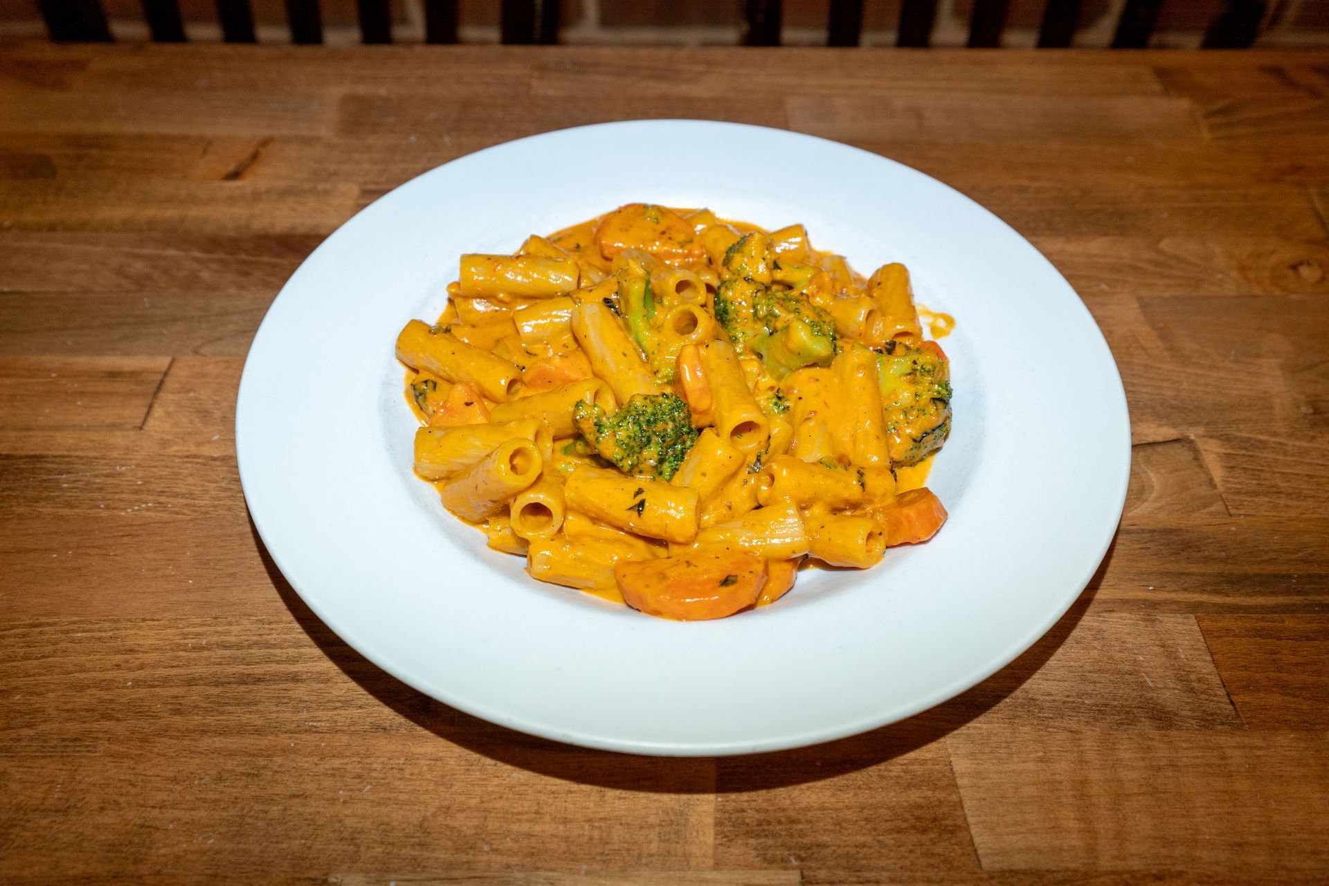 Pasta dish with rigatoni, broccoli, and carrots in a creamy orange sauce, served on a white plate.