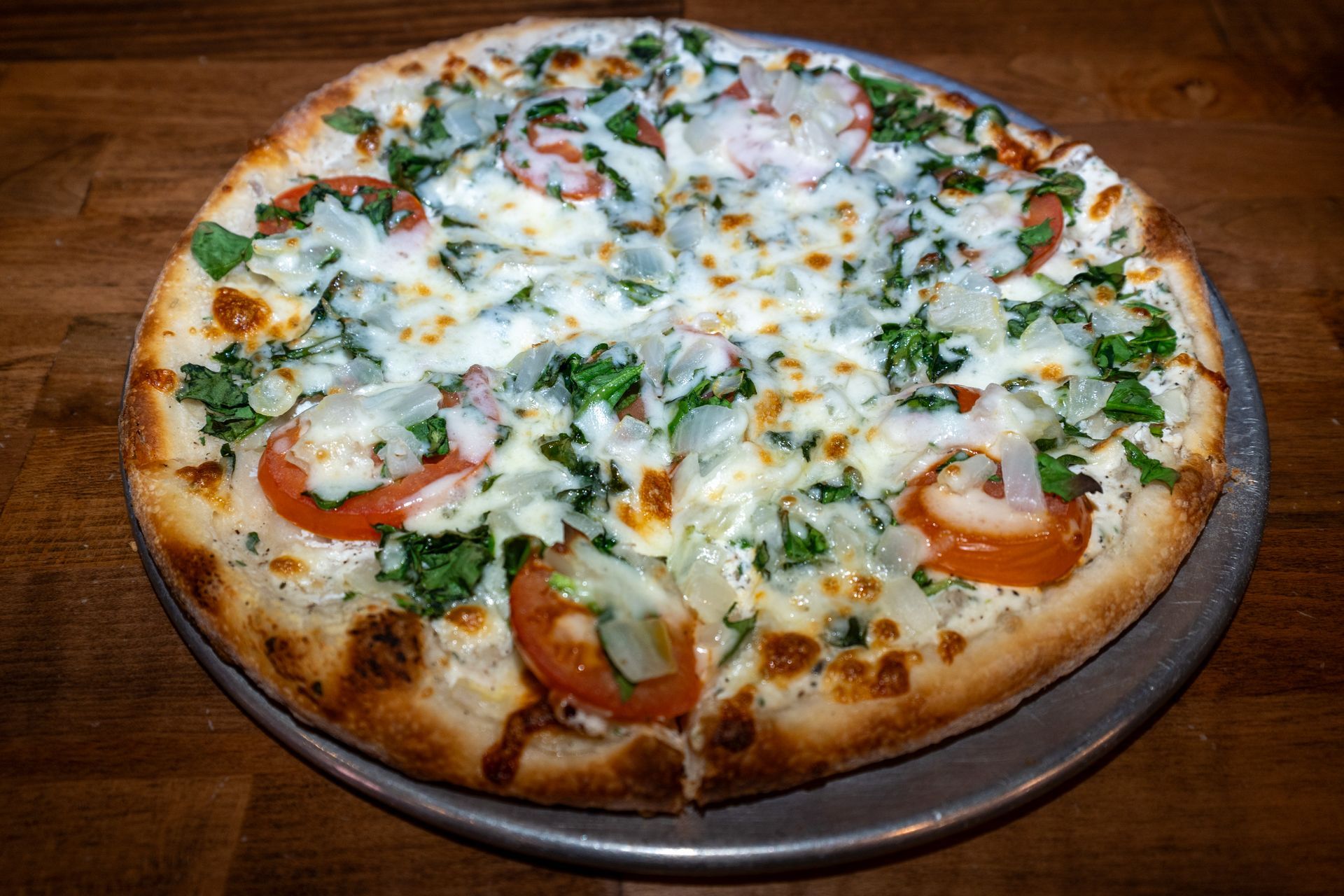 Pizza topped with tomatoes, onions, basil, and melted cheese on a metal pan.