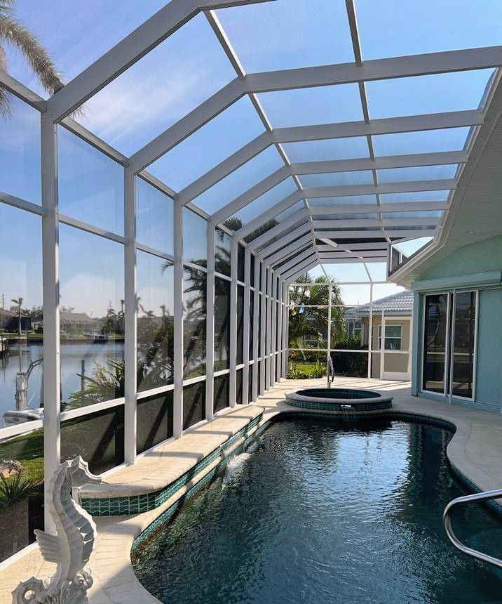 A screened-in swimming pool and spa on a patio overlooking a canal under a clear blue sky.