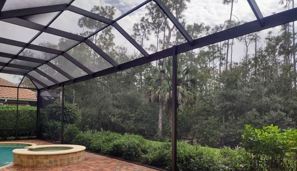 A swimming pool and hot tub enclosed by a screen structure, overlooking a lush green wooded area.