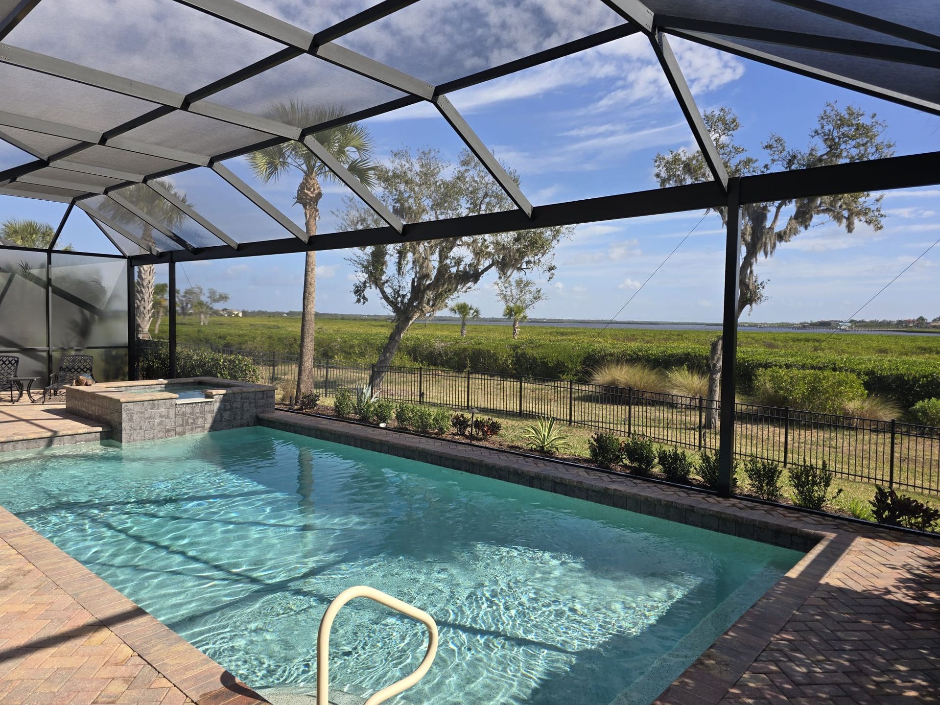 A pool with an attached spa inside a screened-in enclosure, overlooking a scenic landscape of trees and greenery.