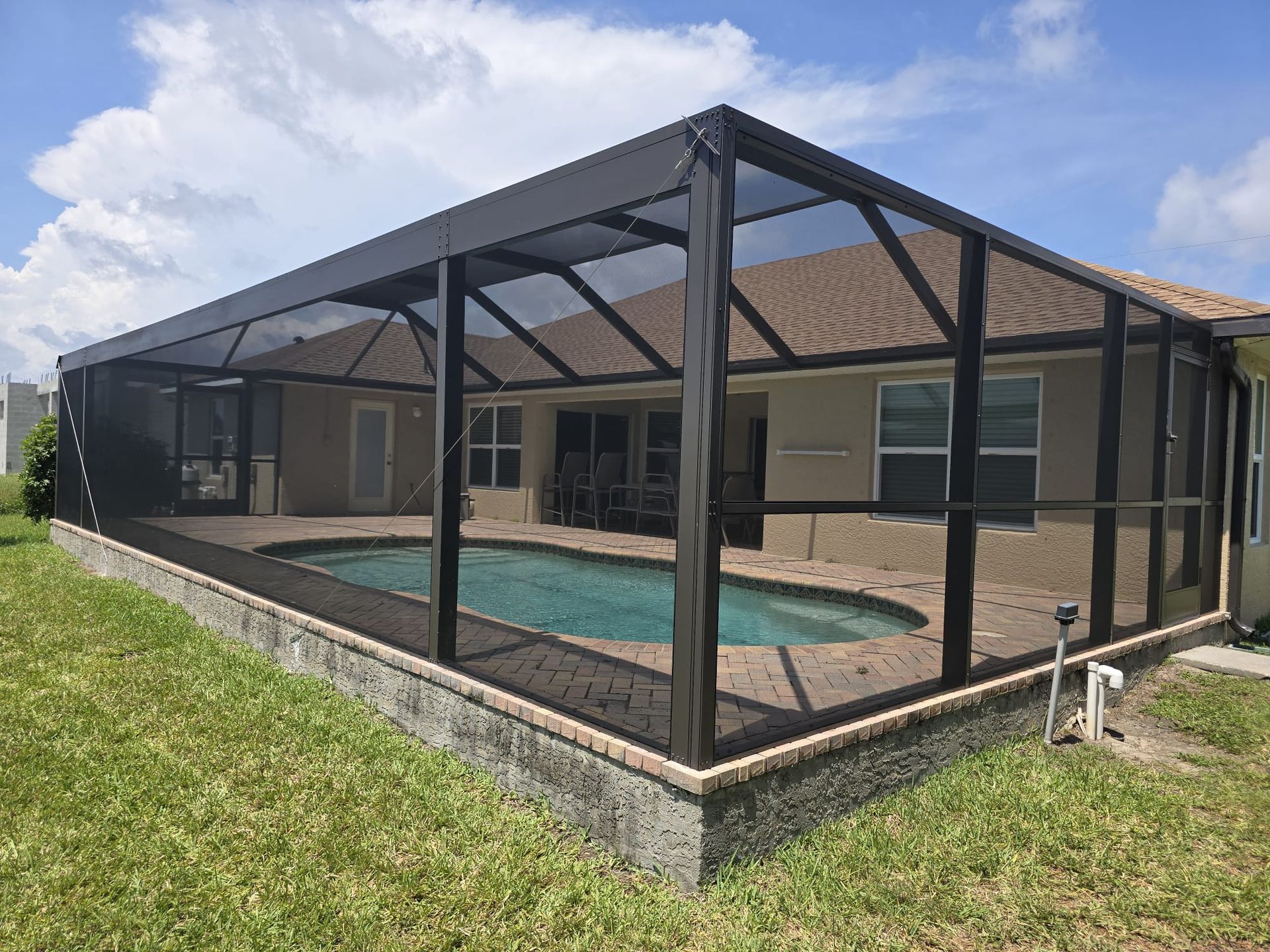 A swimming pool enclosed by a black metal and screen cage attached to the back of a house with a beige exterior.