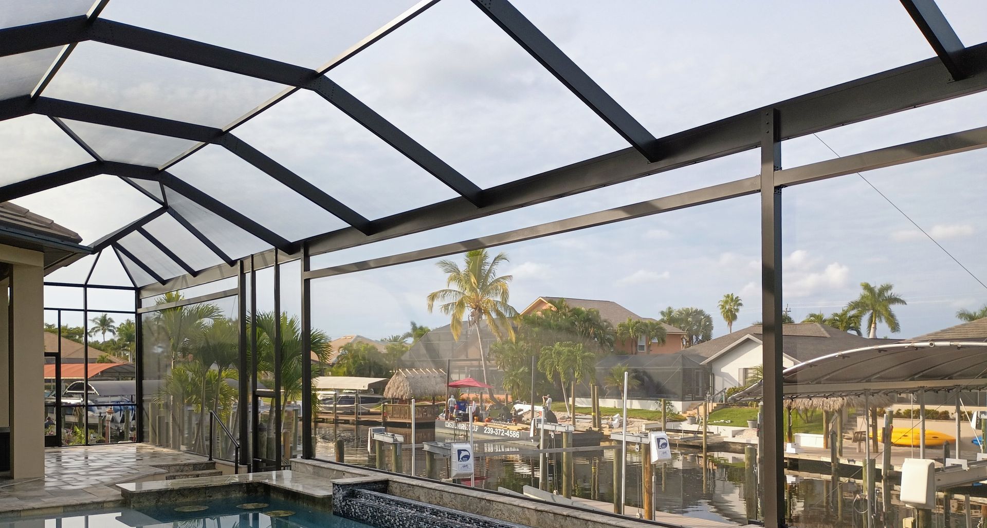 A backyard swimming pool enclosed by a screened-in black metal cage, overlooking a canal with neighboring homes.
