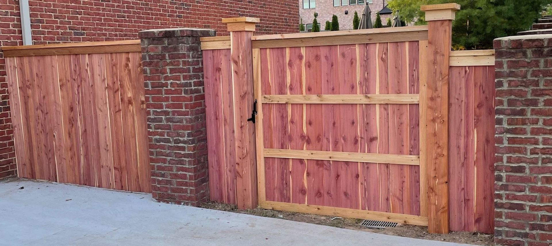 A wooden fence with a gate in front of a brick wall.