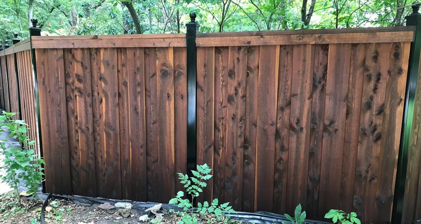A wooden fence with a black post in the middle of a yard.
