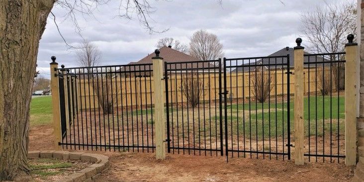 A metal fence with a wooden fence behind it.