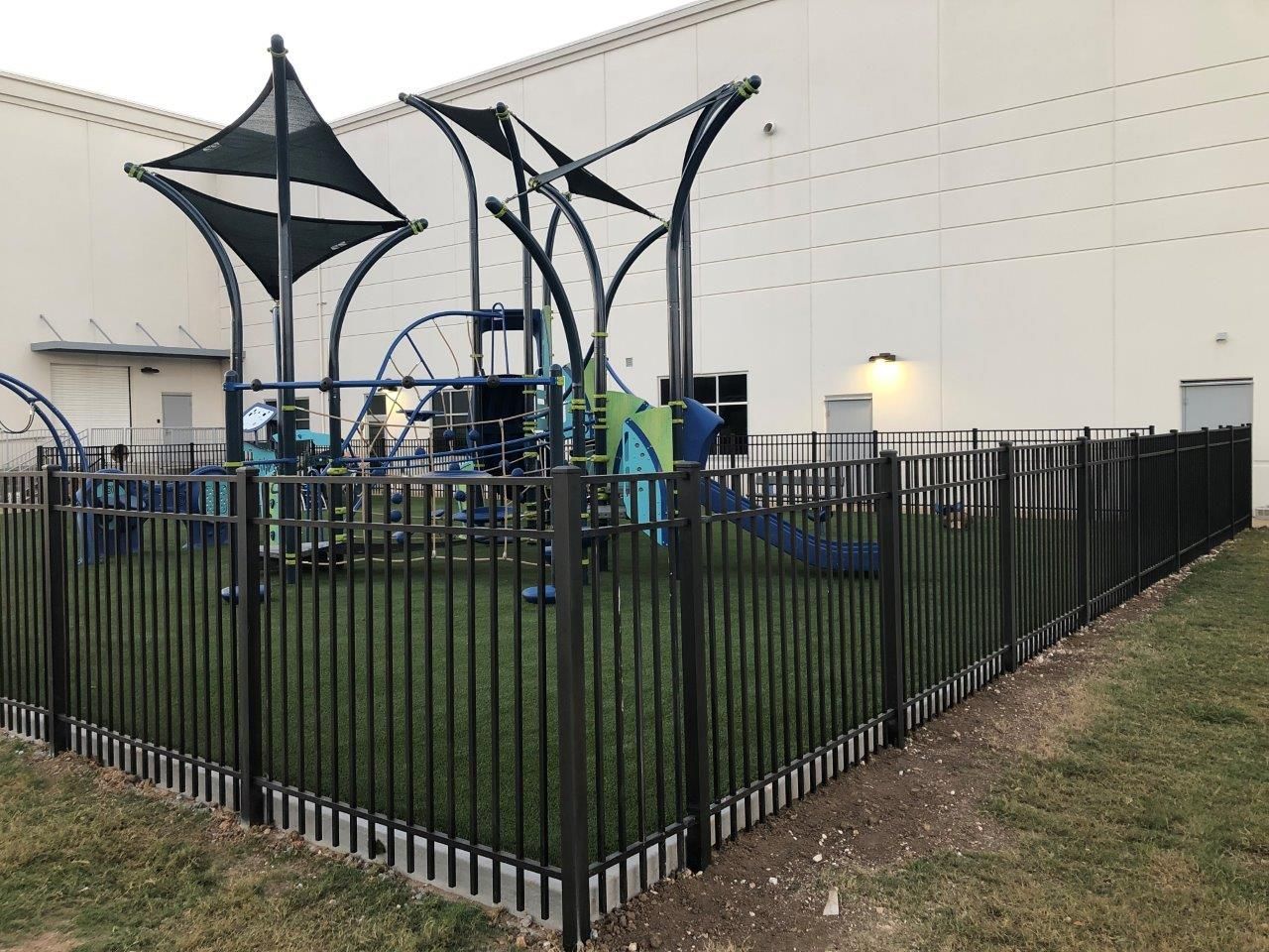 a black fence surrounds a playground with a white building in the background