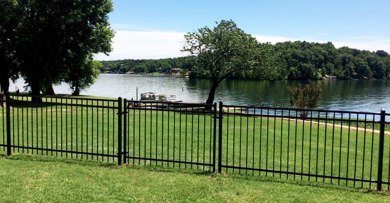 a black fence surrounds a grassy area with a lake in the background